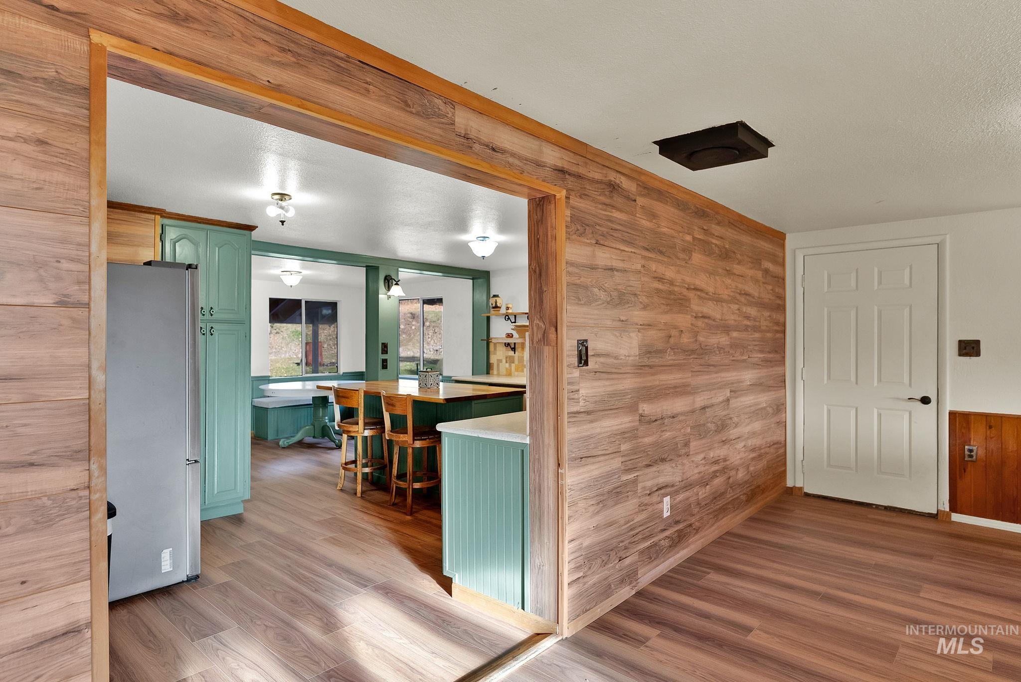 Kitchen featuring green cabinetry, wood walls, freestanding refrigerator, light wood finished floors, and light countertops