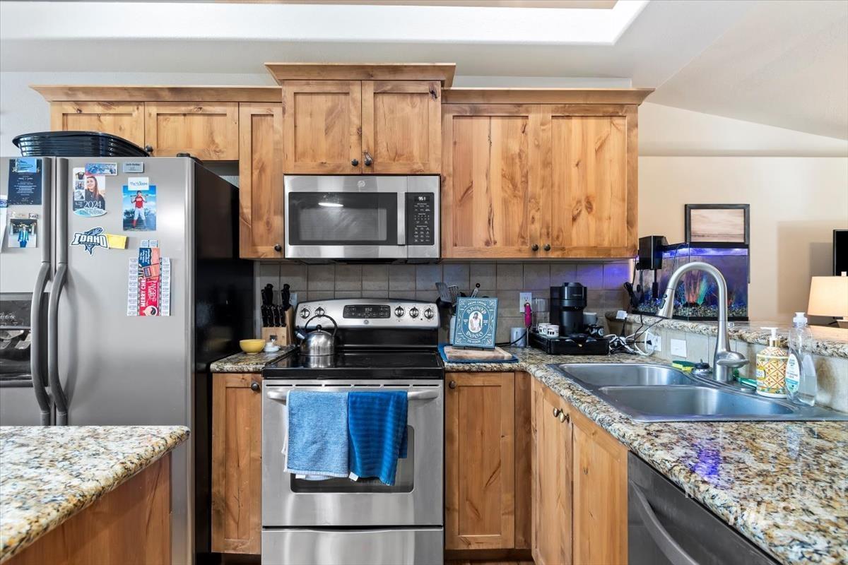 Kitchen with stainless steel appliances, backsplash, light stone countertops, and brown cabinetry
