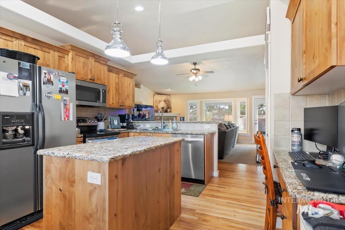 Kitchen with backsplash, stainless steel appliances, a center island, decorative light fixtures, and light wood-style floors