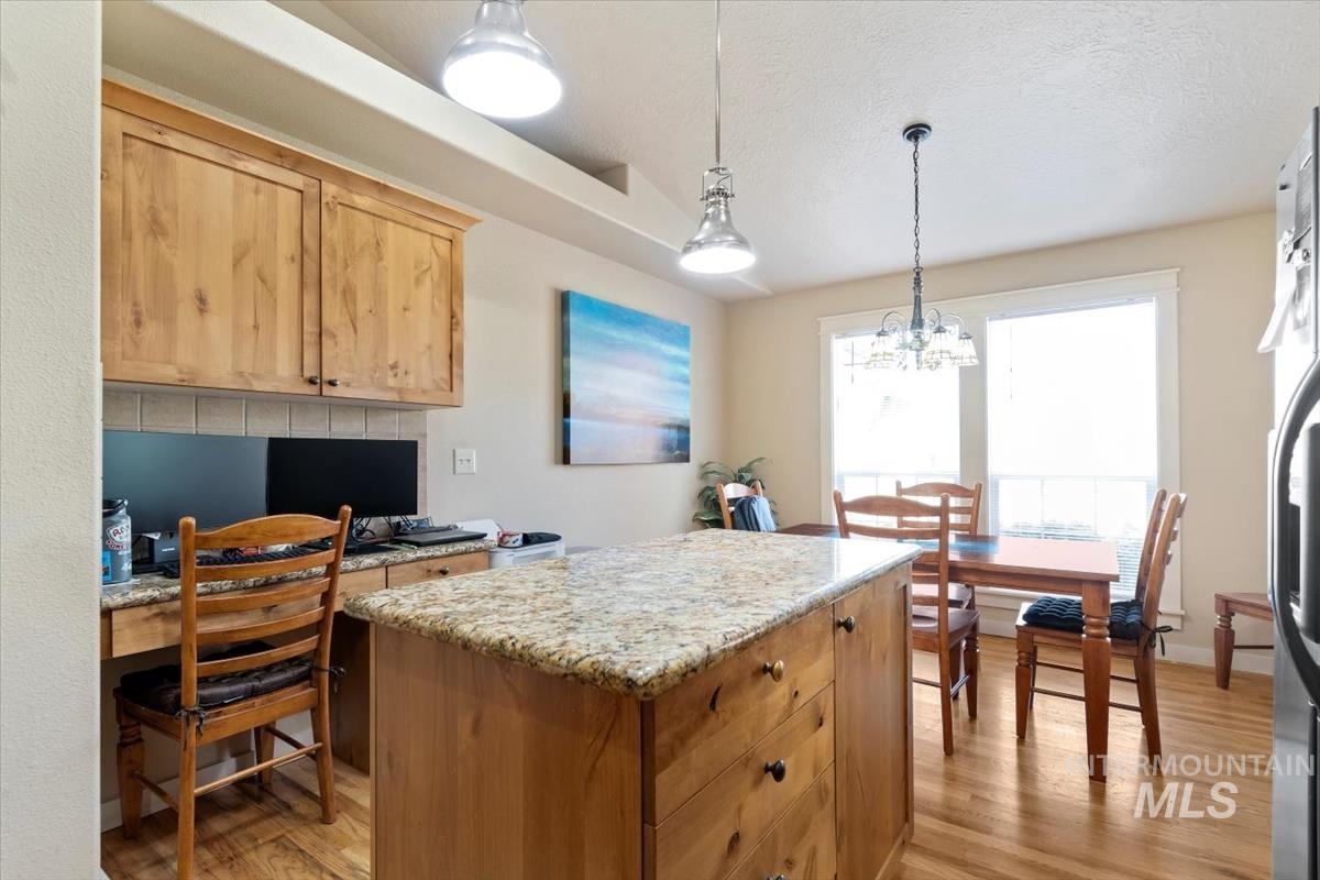 Kitchen with a center island, light wood-type flooring, decorative light fixtures, a textured ceiling, and light stone counters