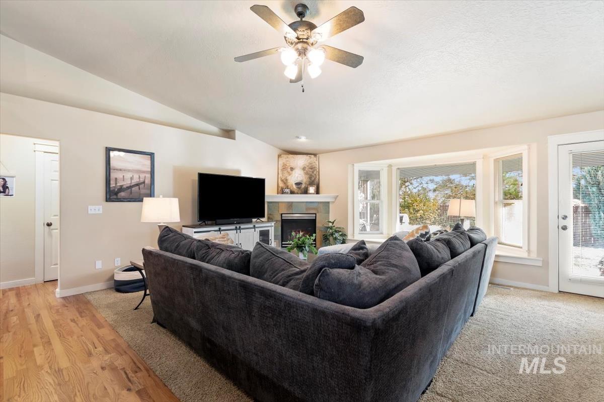 Living room with a fireplace, lofted ceiling, ceiling fan, and light wood-style flooring