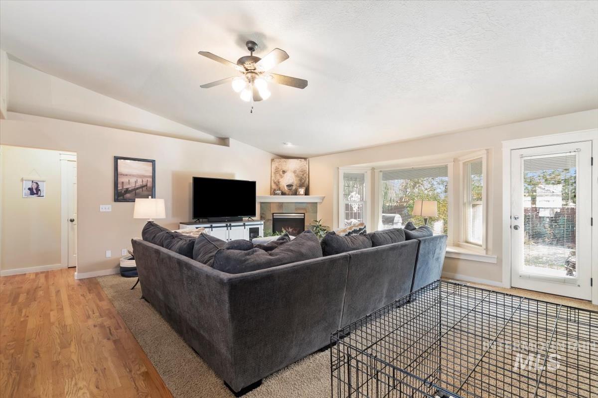 Living room featuring a warm lit fireplace, light wood-type flooring, vaulted ceiling, and a ceiling fan