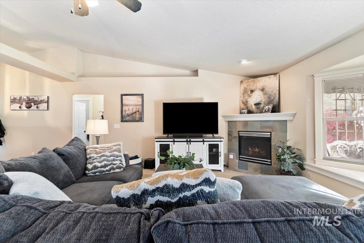Carpeted living room with vaulted ceiling, a fireplace, and a ceiling fan