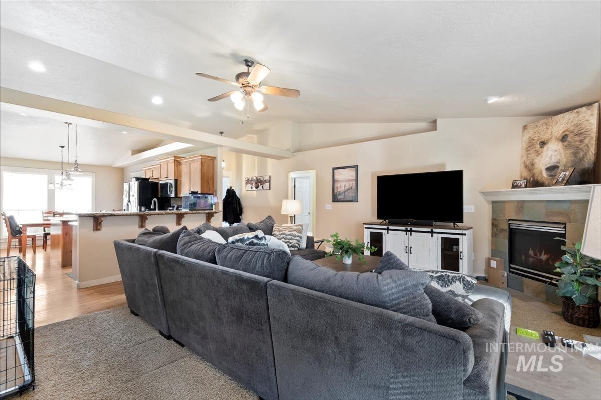 Living room with a tile fireplace, vaulted ceiling, recessed lighting, a ceiling fan, and light wood-style floors
