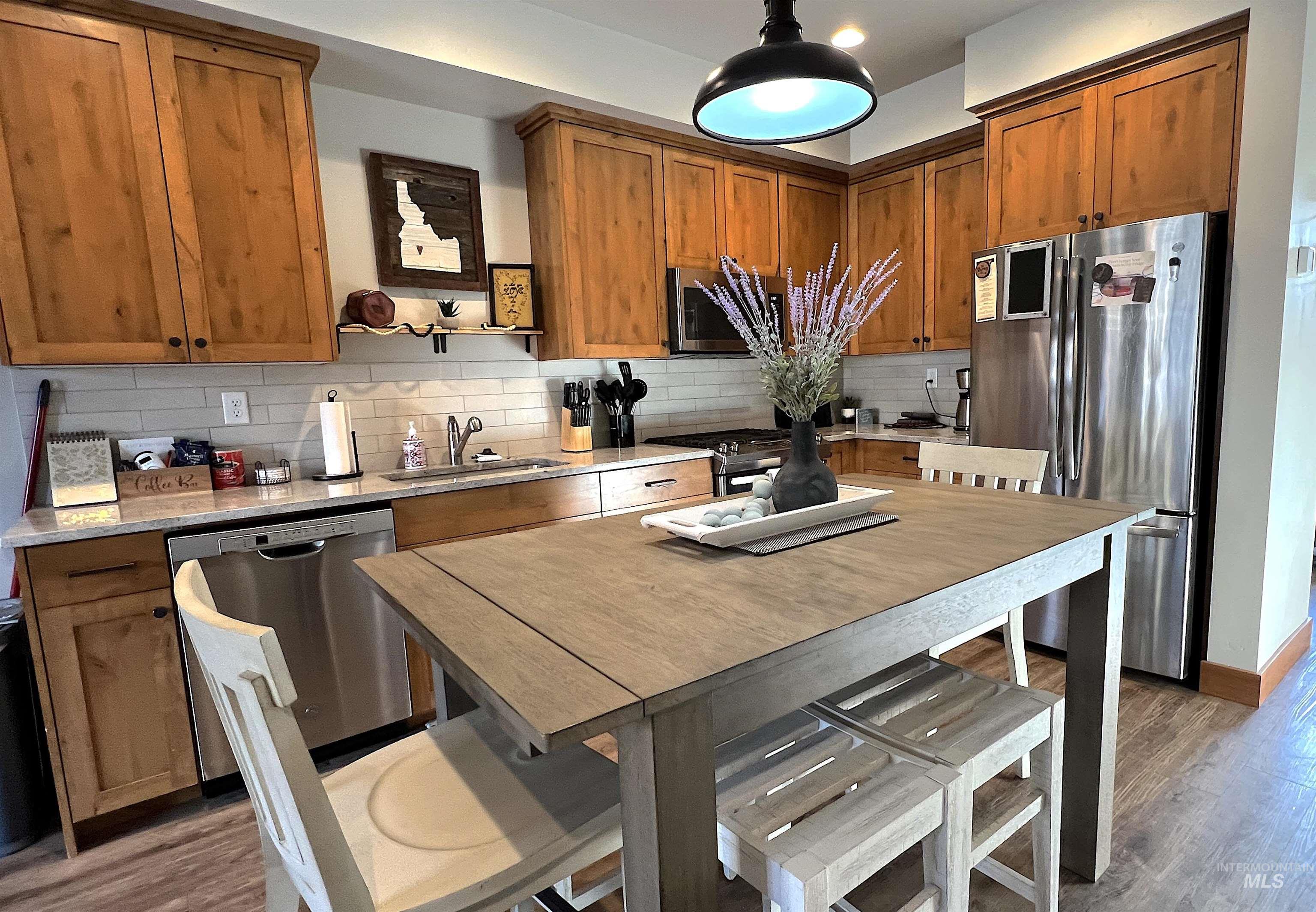 Kitchen featuring wood finished floors, stainless steel appliances, brown cabinetry, and decorative backsplash