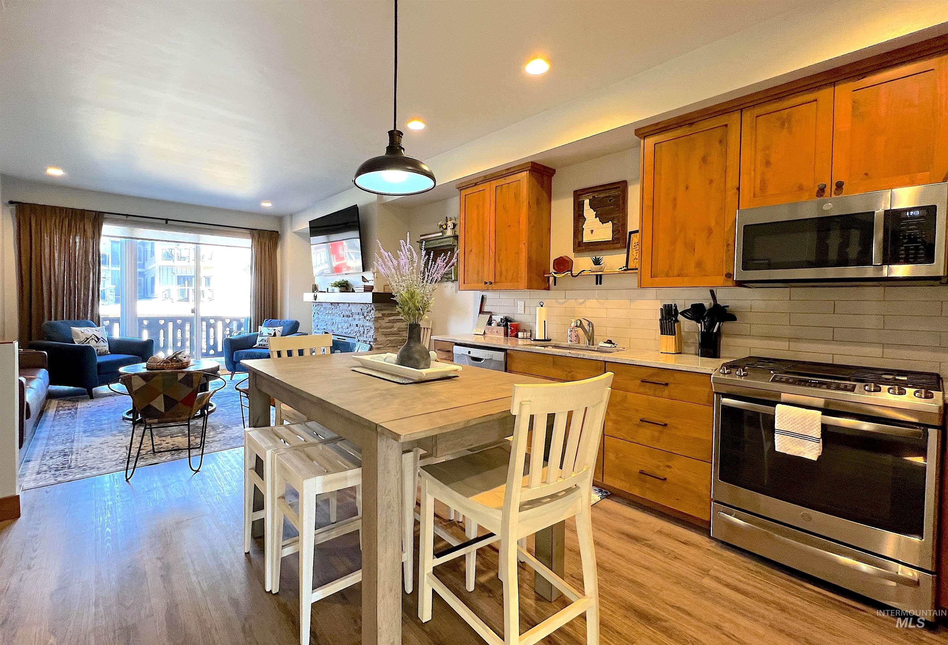 Kitchen with stainless steel appliances, brown cabinets, decorative backsplash, open floor plan, and pendant lighting