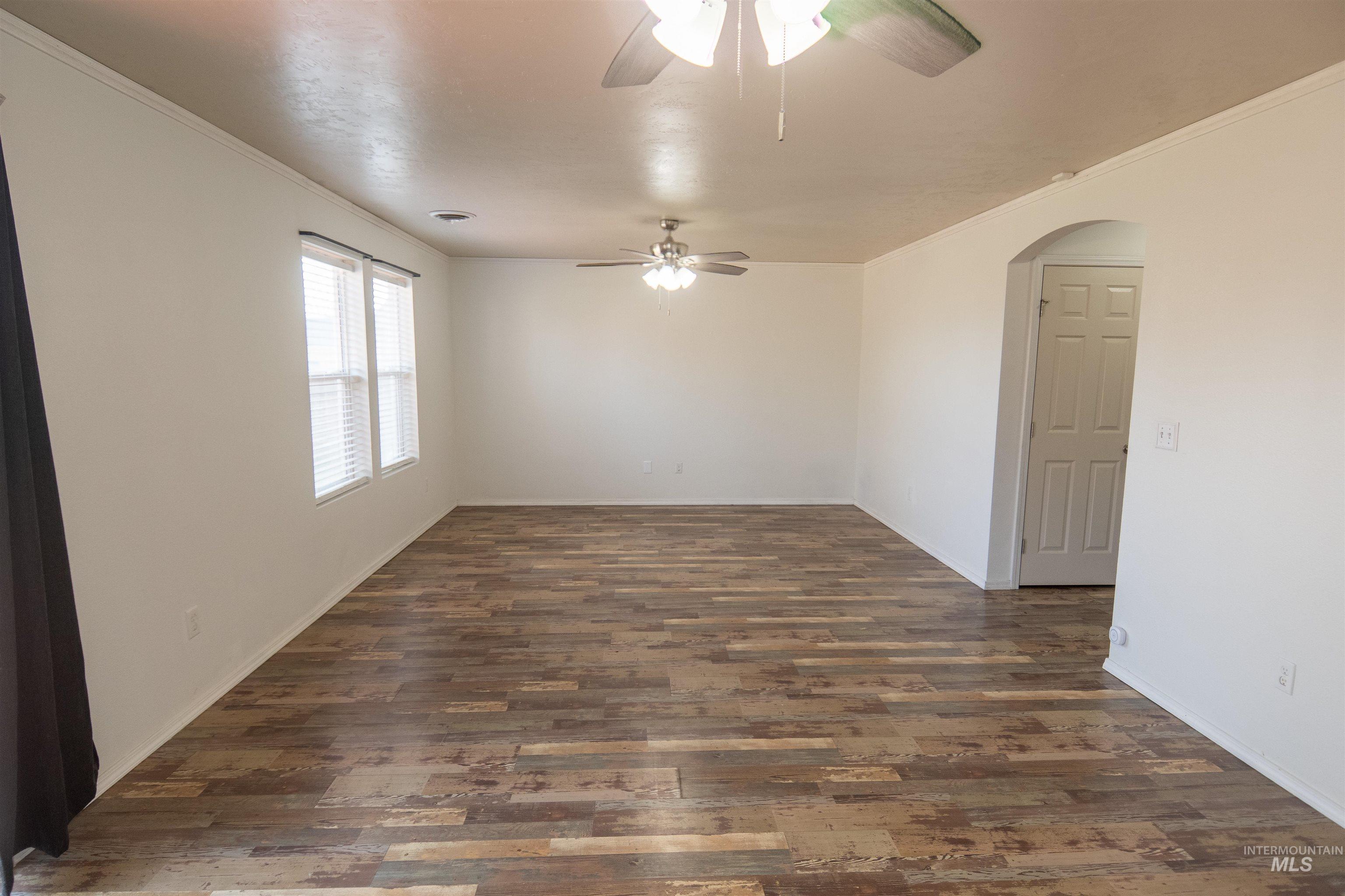 Empty room featuring ornamental molding, arched walkways, and dark wood-style floors