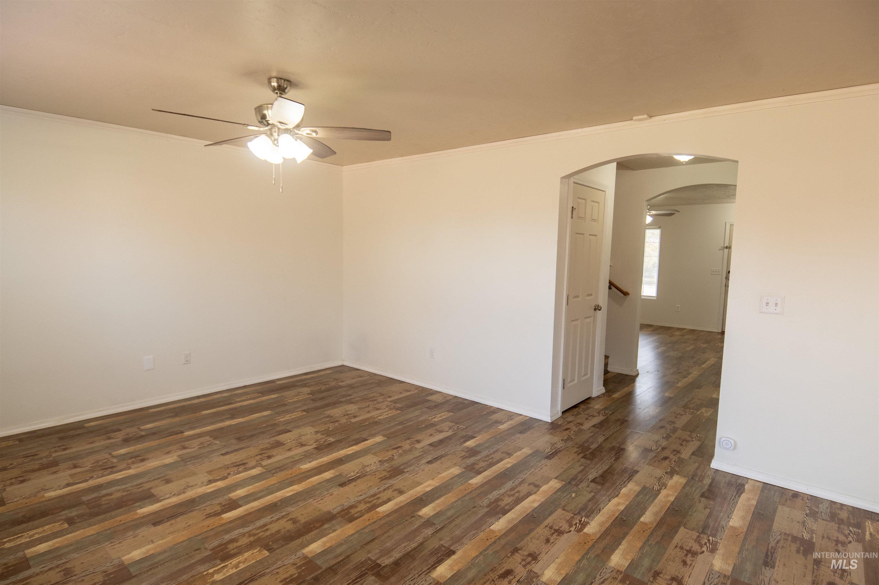Empty room featuring ceiling fan, ornamental molding, arched walkways, and dark wood-type flooring
