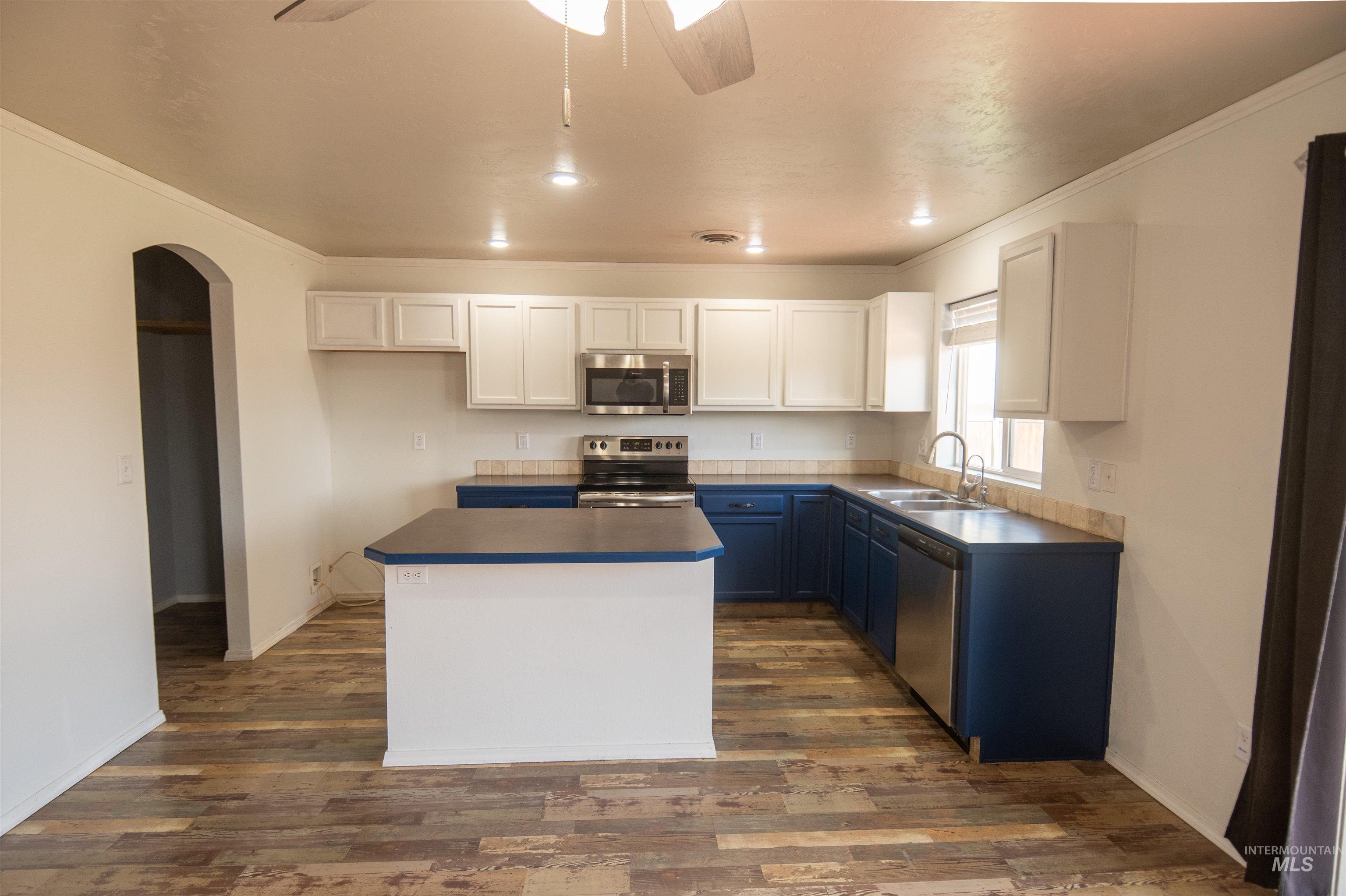 Kitchen with white cabinets, dark countertops, a ceiling fan, crown molding, and stainless steel appliances