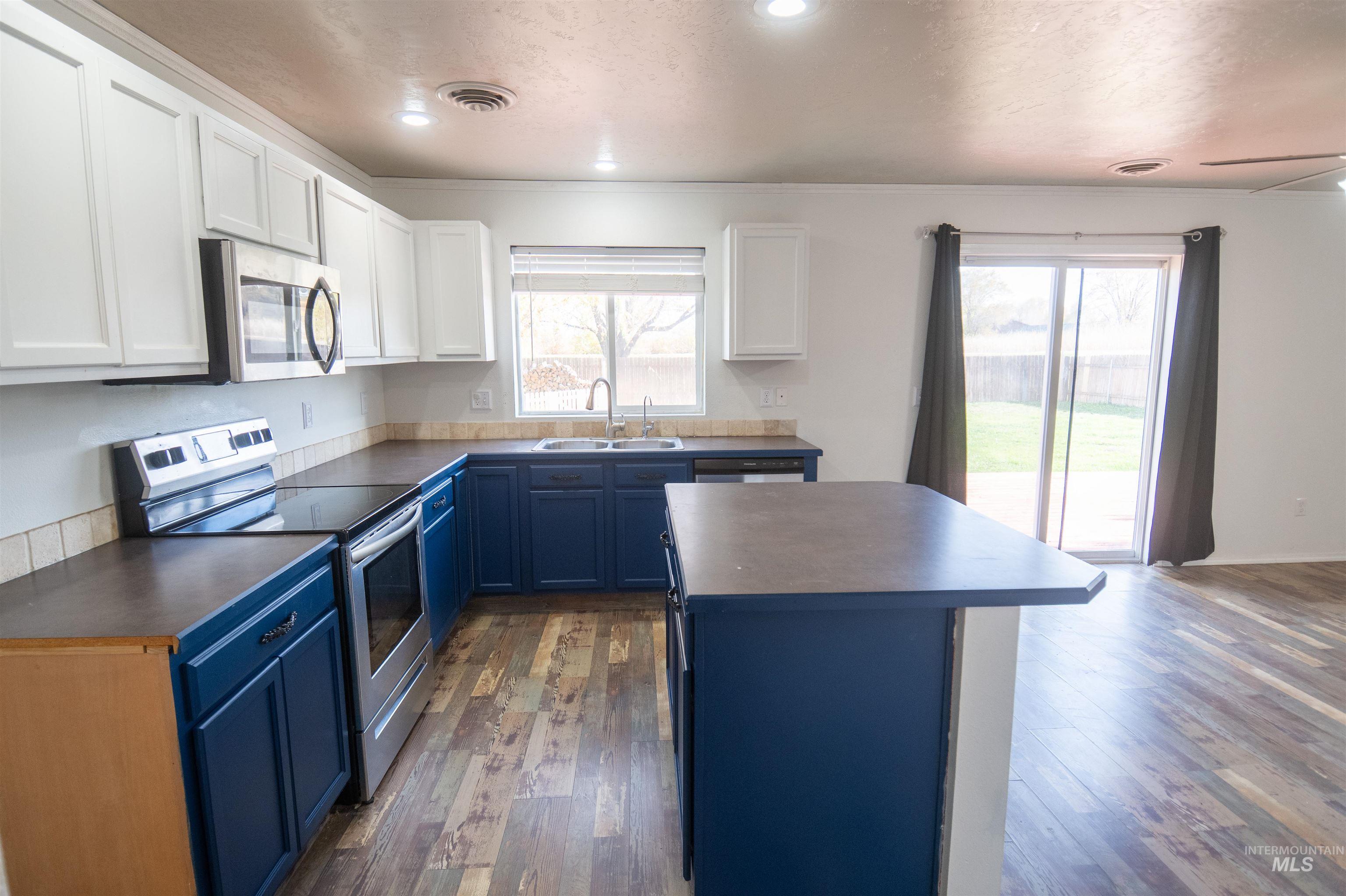 Kitchen with appliances with stainless steel finishes, white cabinetry, blue cabinetry, dark wood-style flooring, and crown molding