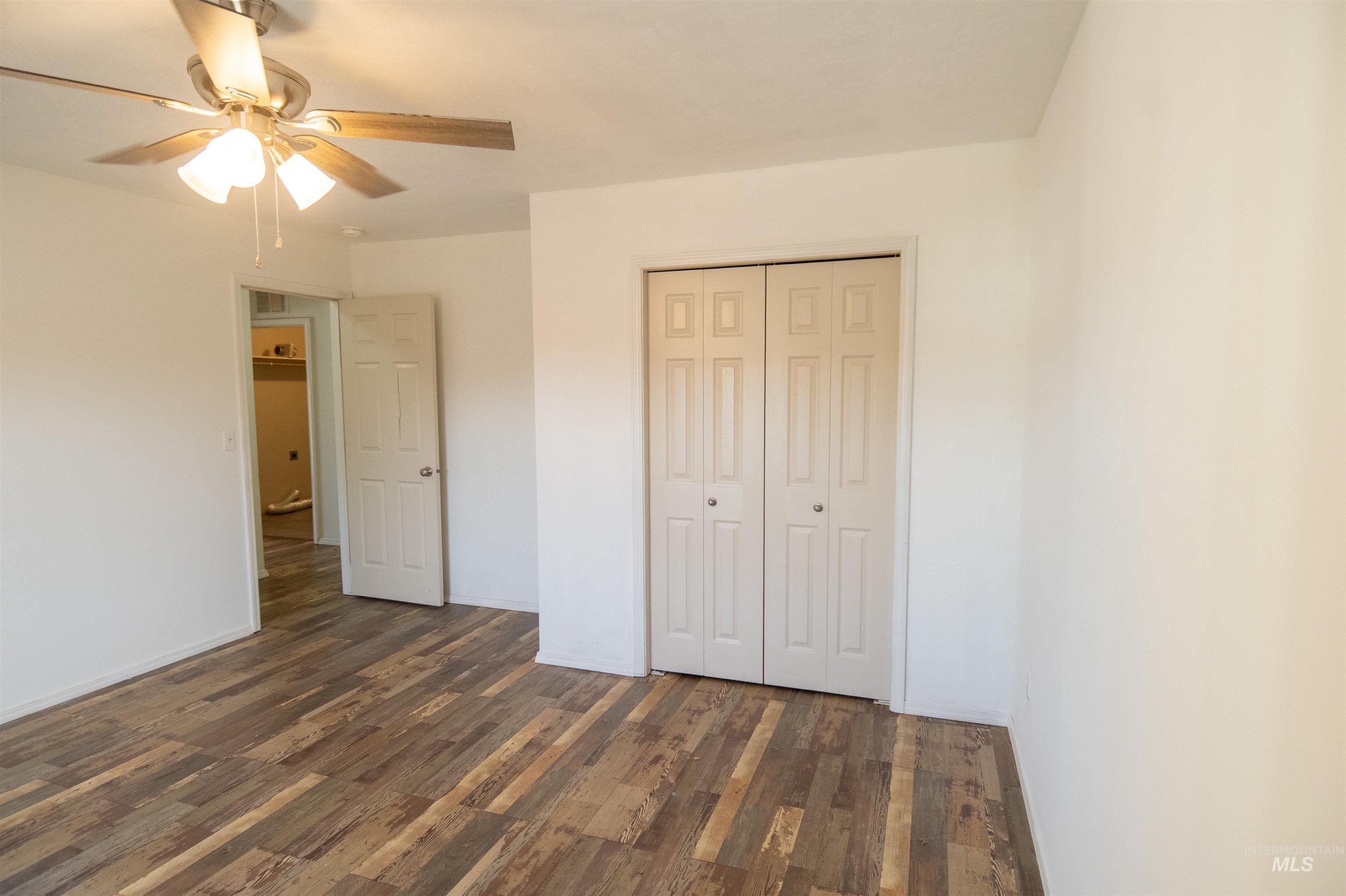 Unfurnished bedroom featuring dark wood-type flooring, a closet, and a ceiling fan