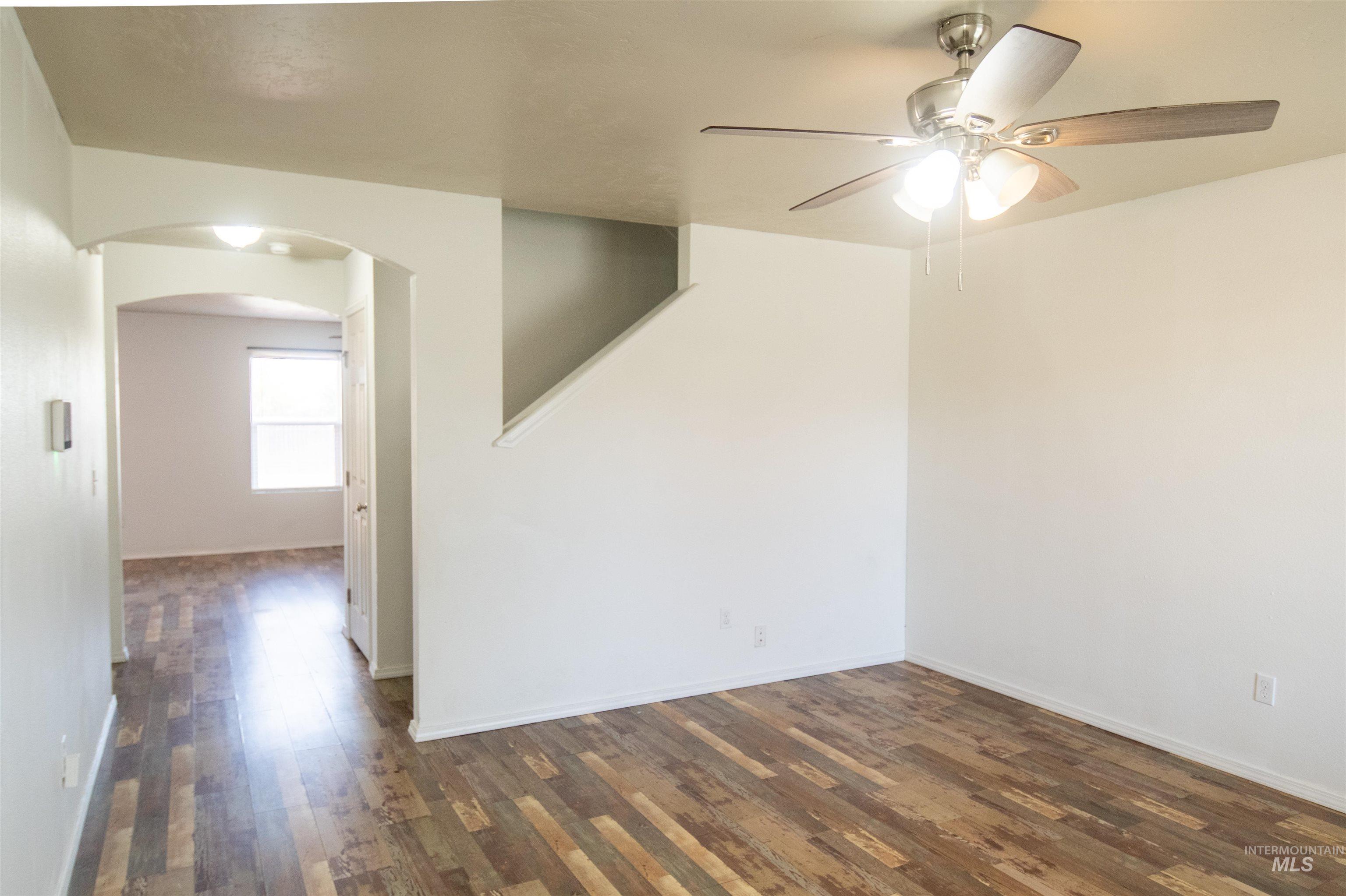 Unfurnished room featuring dark wood-style floors, arched walkways, and a ceiling fan