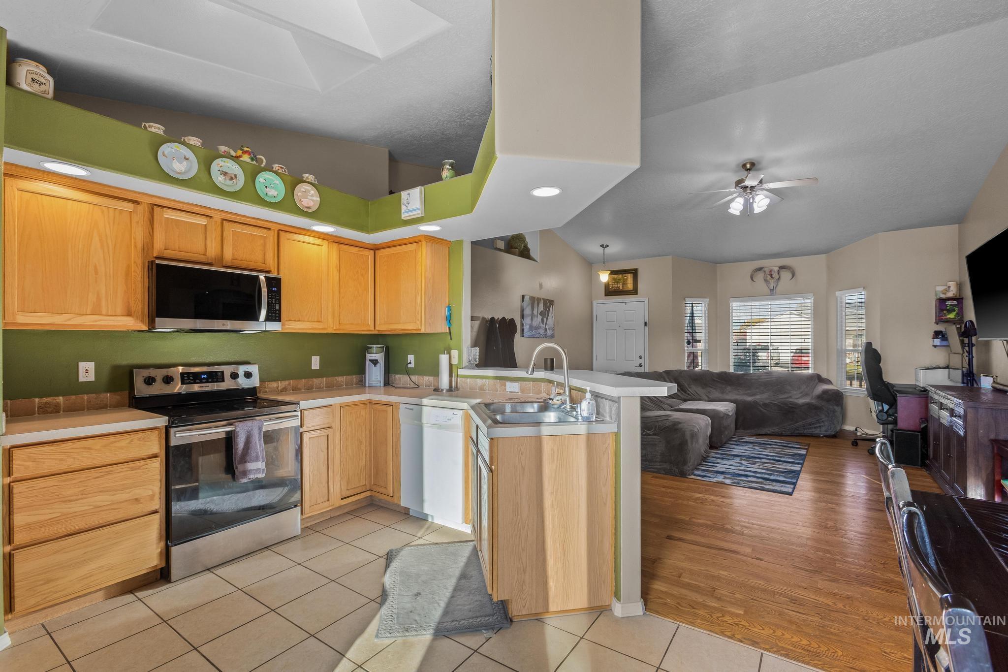 Kitchen featuring stainless steel appliances, open floor plan, light countertops, a peninsula, and light tile patterned floors