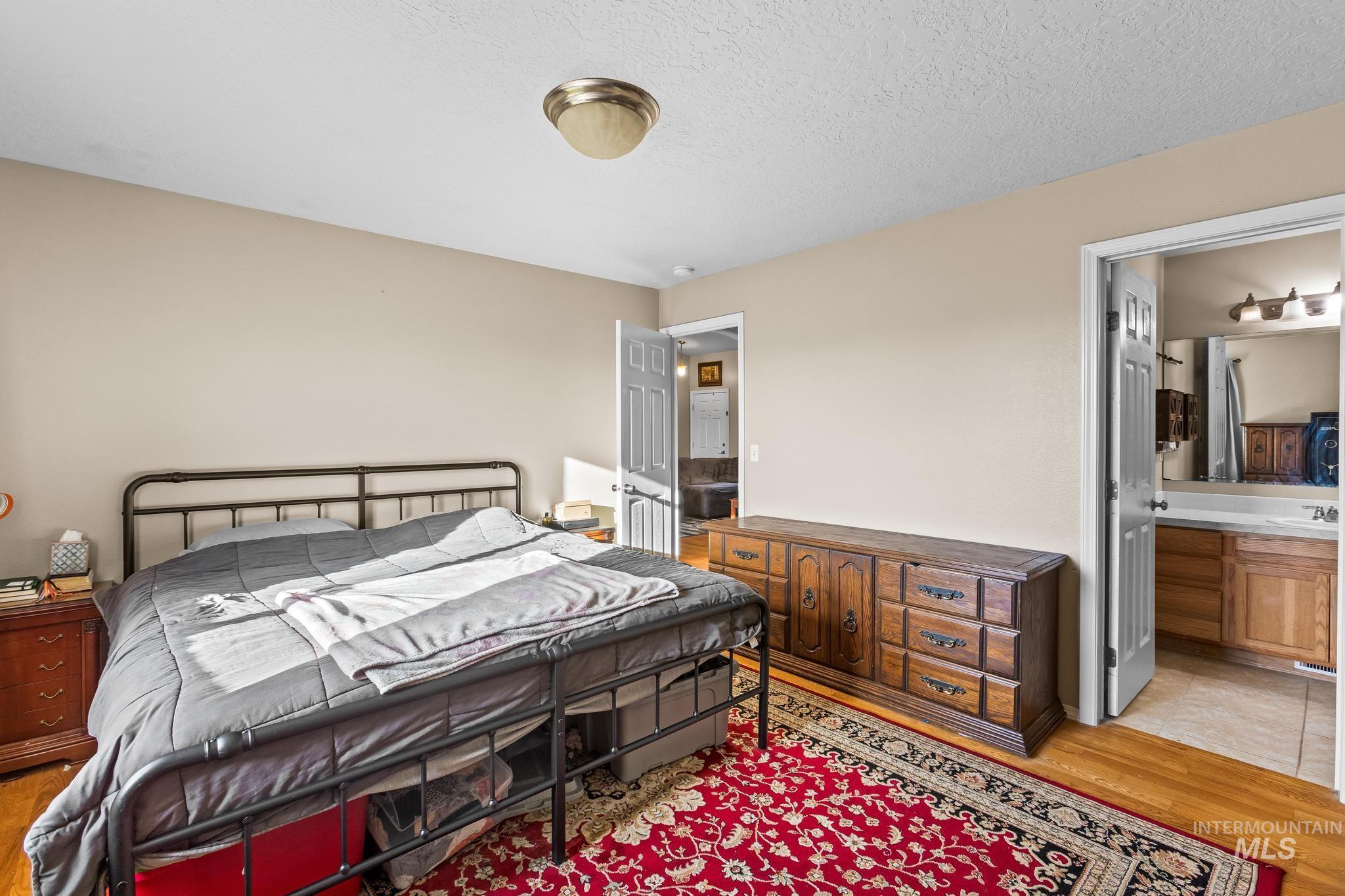 Bedroom with light wood-style flooring, a textured ceiling, and ensuite bath