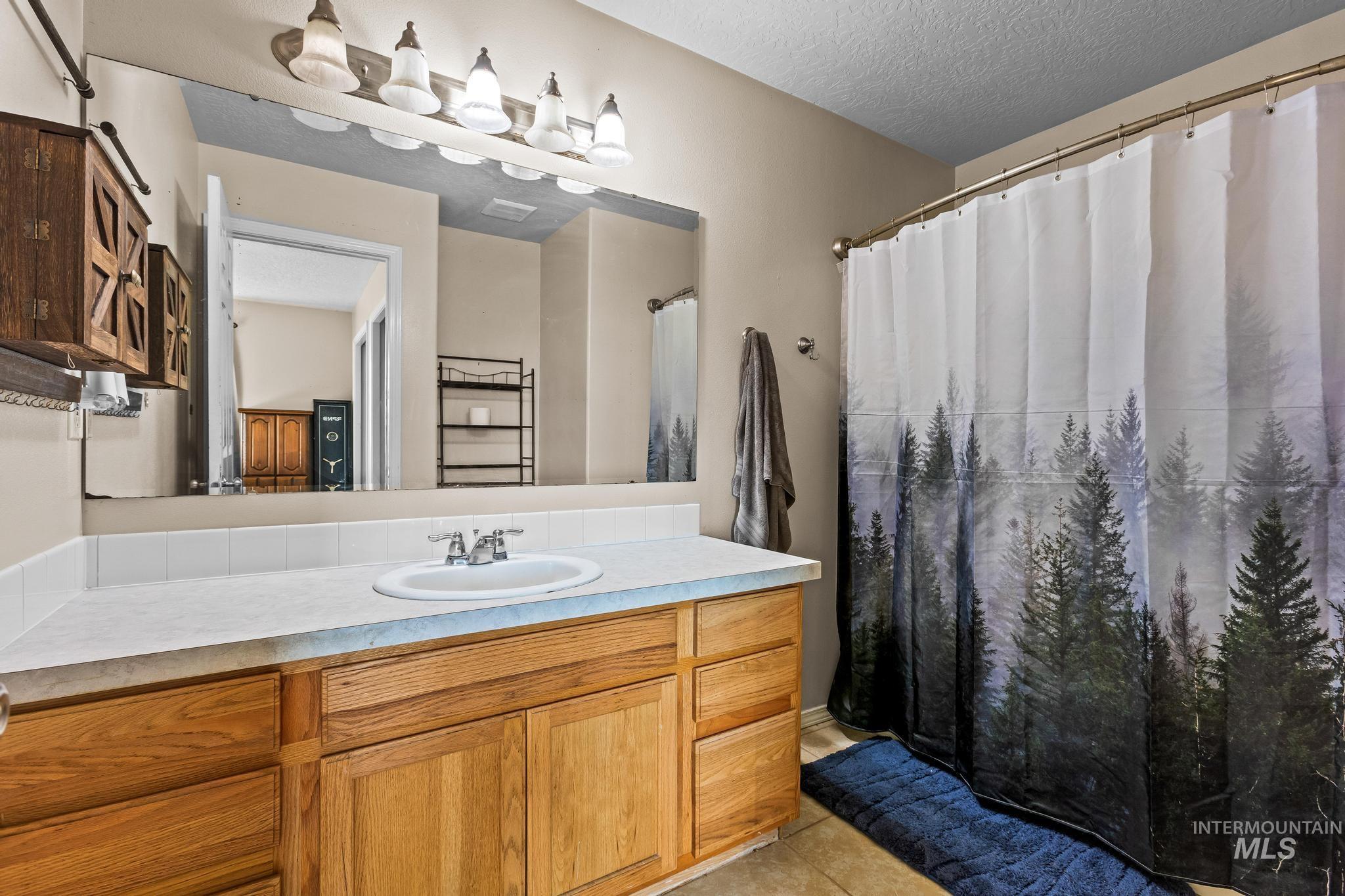 Bathroom featuring curtained shower, vanity, a textured ceiling, light tile patterned floors, and a towel warming rack
