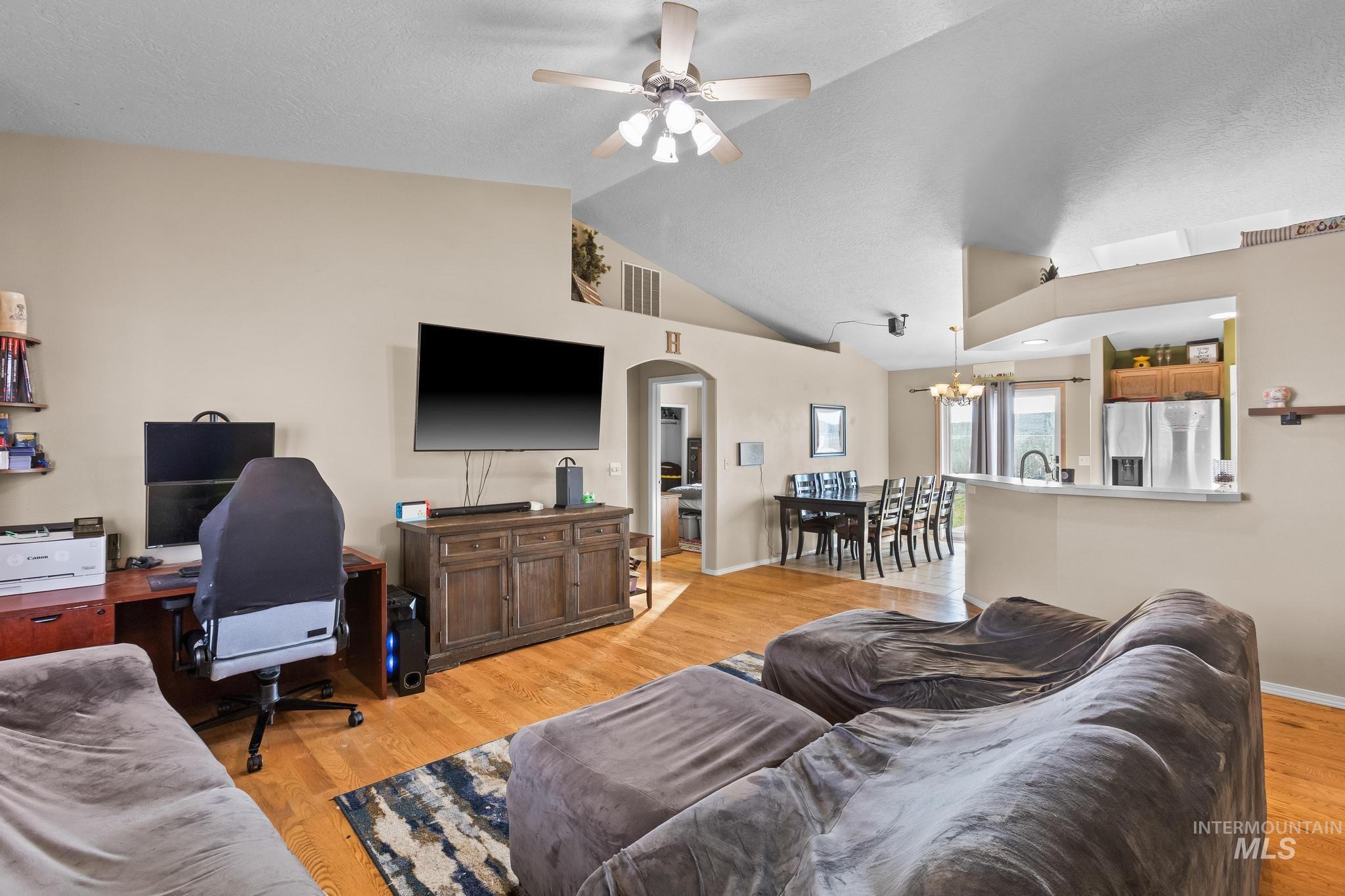 Living area featuring light wood-style floors, vaulted ceiling, arched walkways, ceiling fan, and a desk