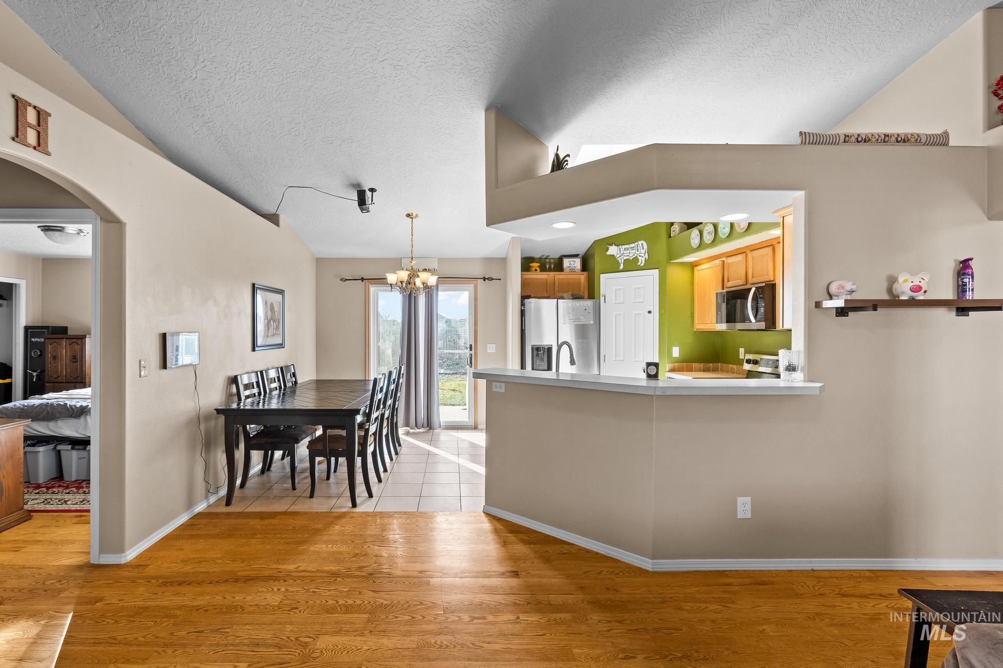 Kitchen with a textured ceiling, arched walkways, light wood-style flooring, a chandelier, and appliances with stainless steel finishes