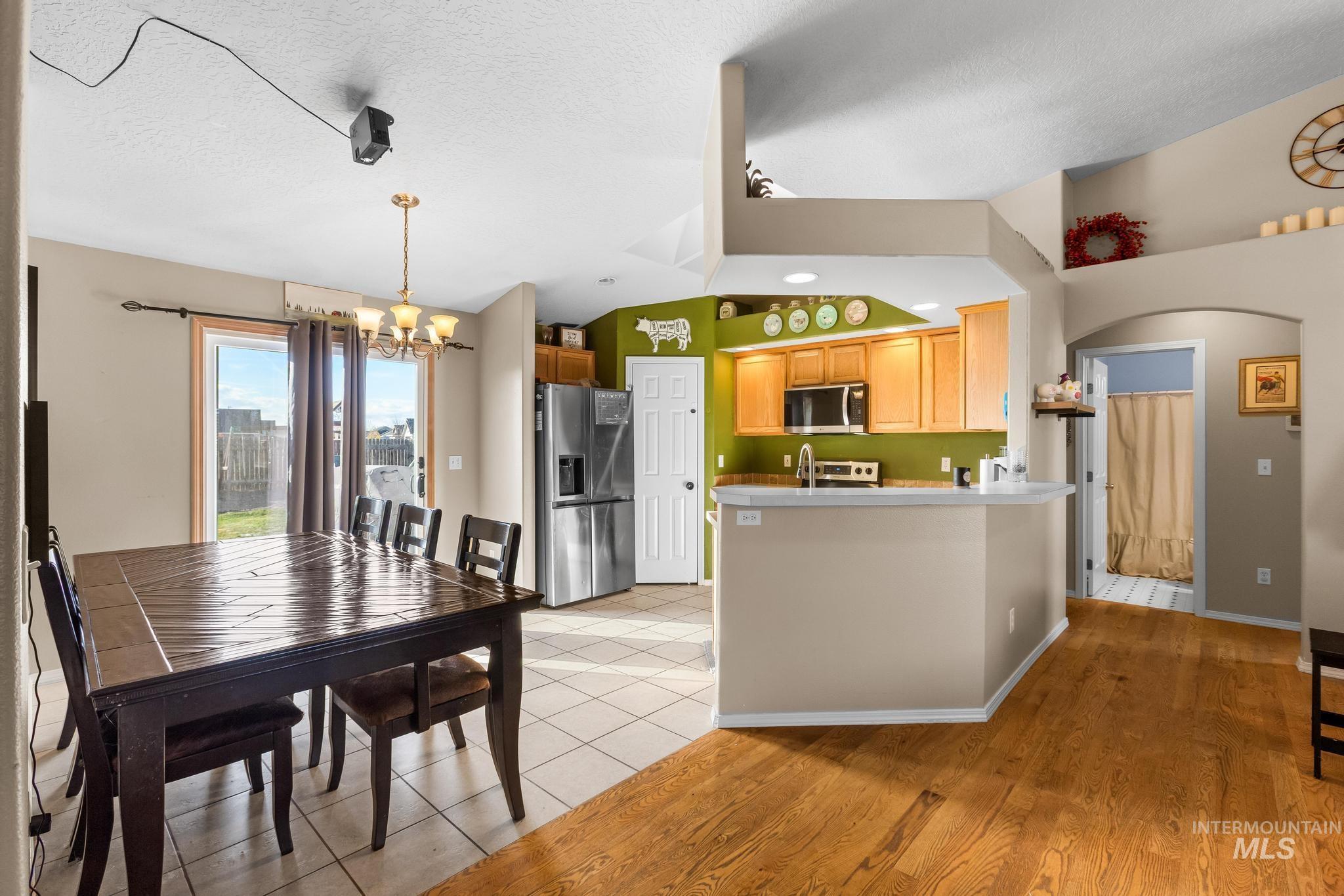 Kitchen featuring appliances with stainless steel finishes, light wood-style floors, a peninsula, light countertops, and a chandelier