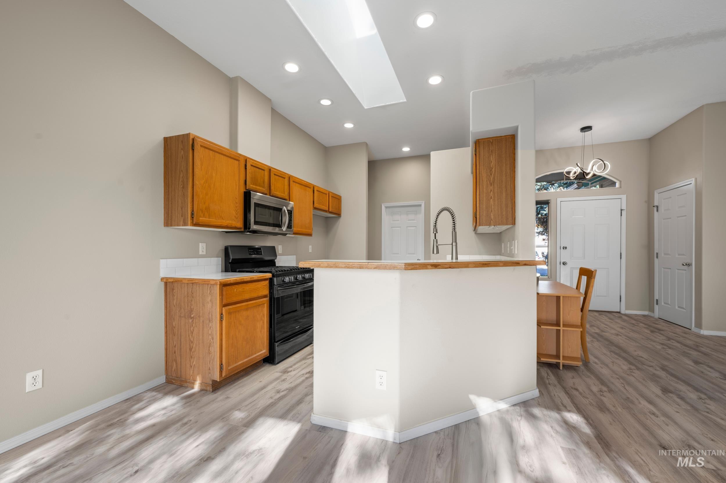 Kitchen with black gas range, recessed lighting, light countertops, a skylight, and light wood finished floors
