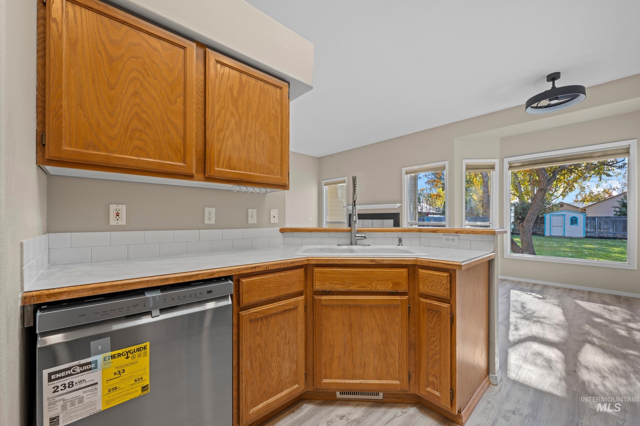 Kitchen with stainless steel dishwasher, brown cabinets, light wood-type flooring, and a peninsula