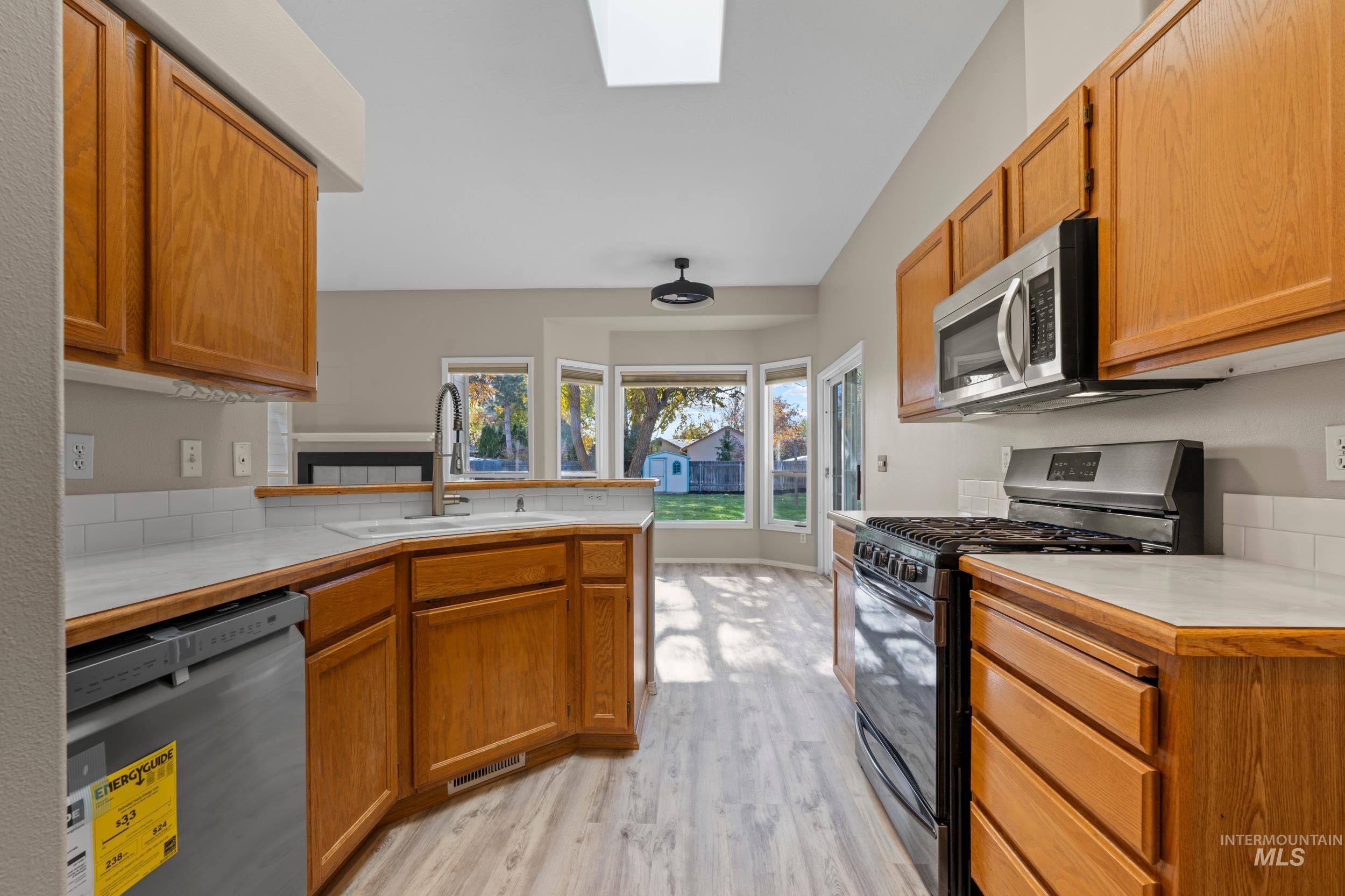 Kitchen featuring light countertops, appliances with stainless steel finishes, light wood-style flooring, brown cabinets, and a peninsula