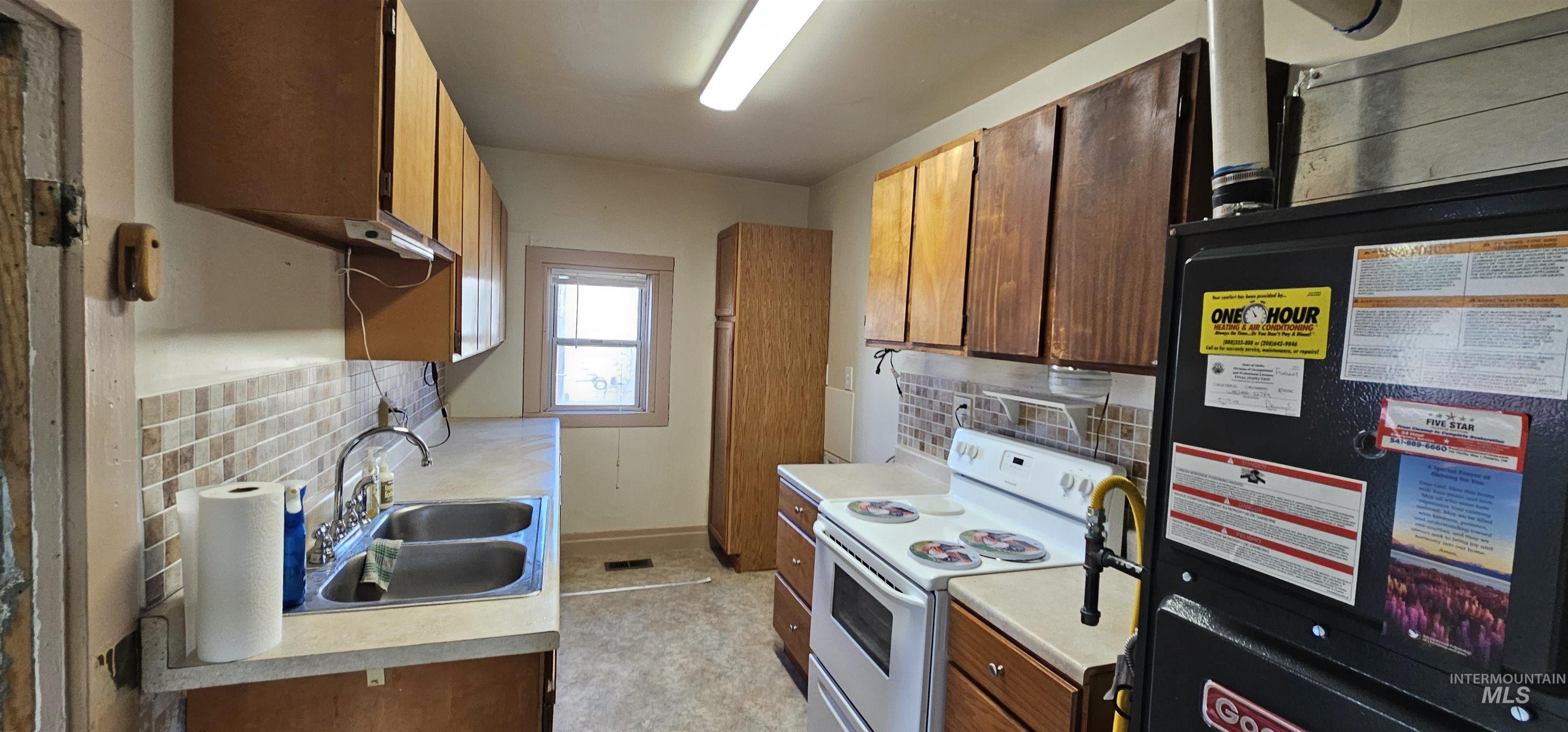 Kitchen featuring white range with electric cooktop, light countertops, heating unit, brown cabinetry, and decorative backsplash
