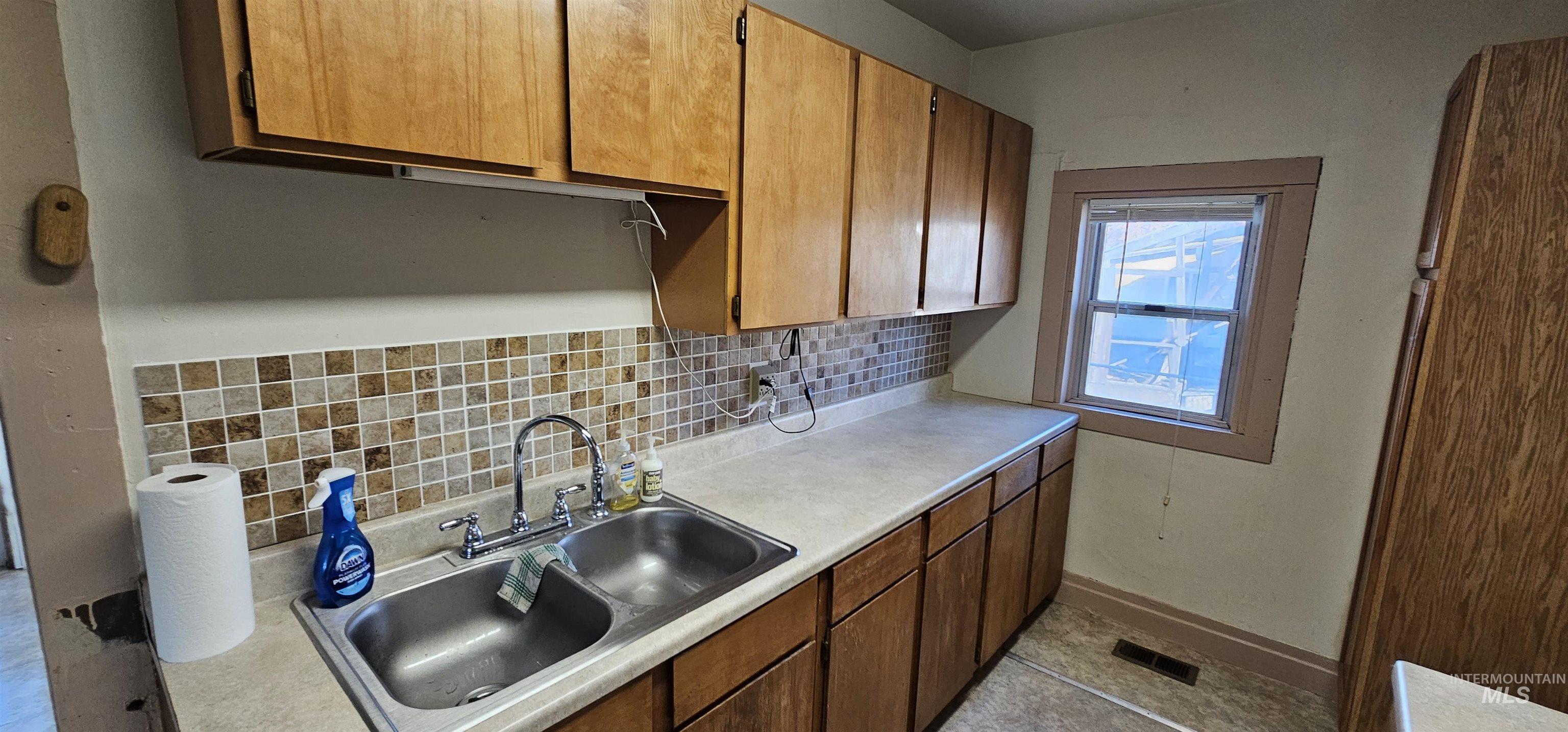 Kitchen with backsplash, light countertops, brown cabinets, and light tile patterned flooring