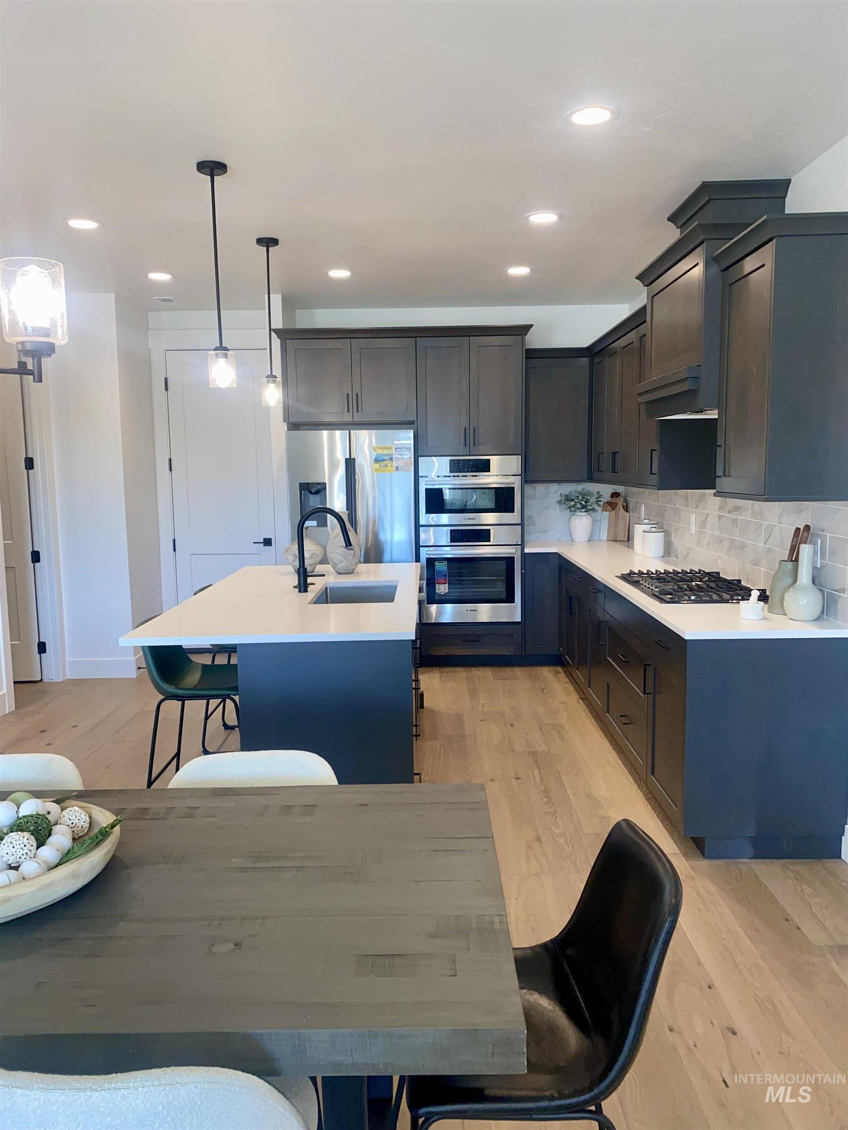 Kitchen featuring a breakfast bar, a center island with sink, decorative backsplash, decorative light fixtures, and light wood-style flooring