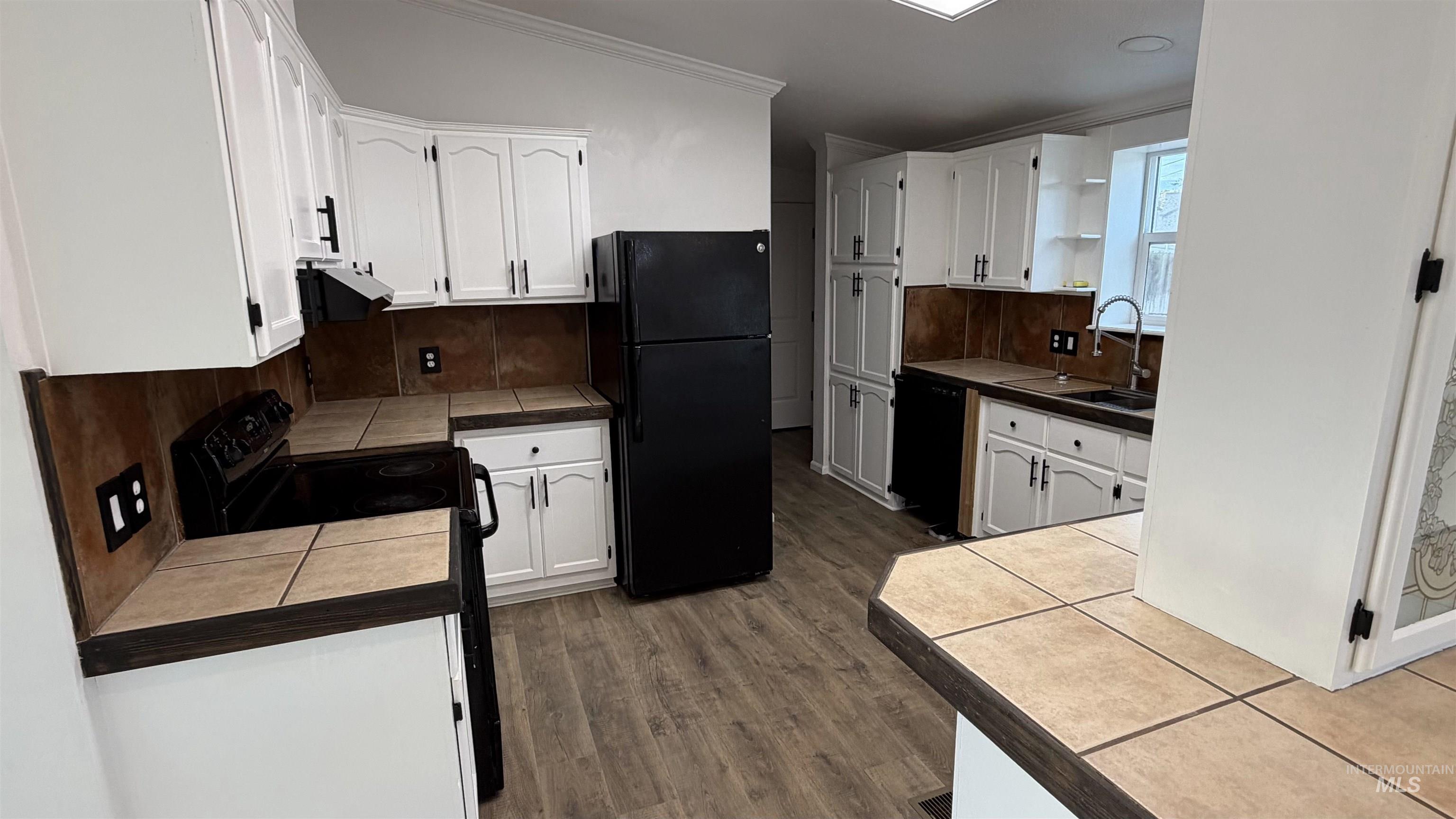Kitchen featuring white cabinets, black appliances, decorative backsplash, dark wood-type flooring, and ornamental molding