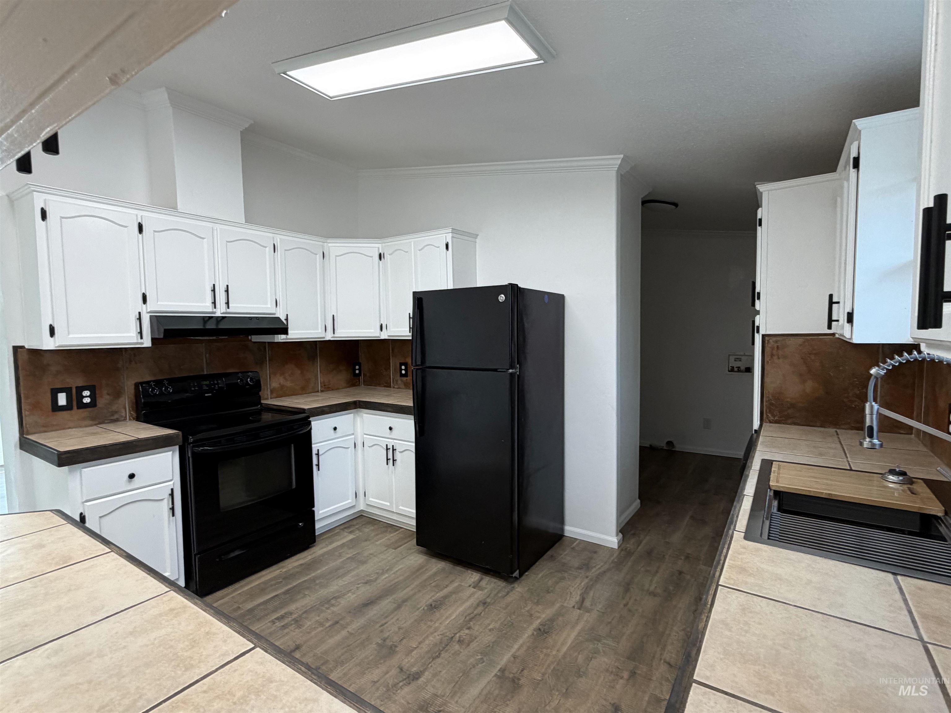 Kitchen with white cabinetry, black appliances, tasteful backsplash, dark wood-style flooring, and tile countertops