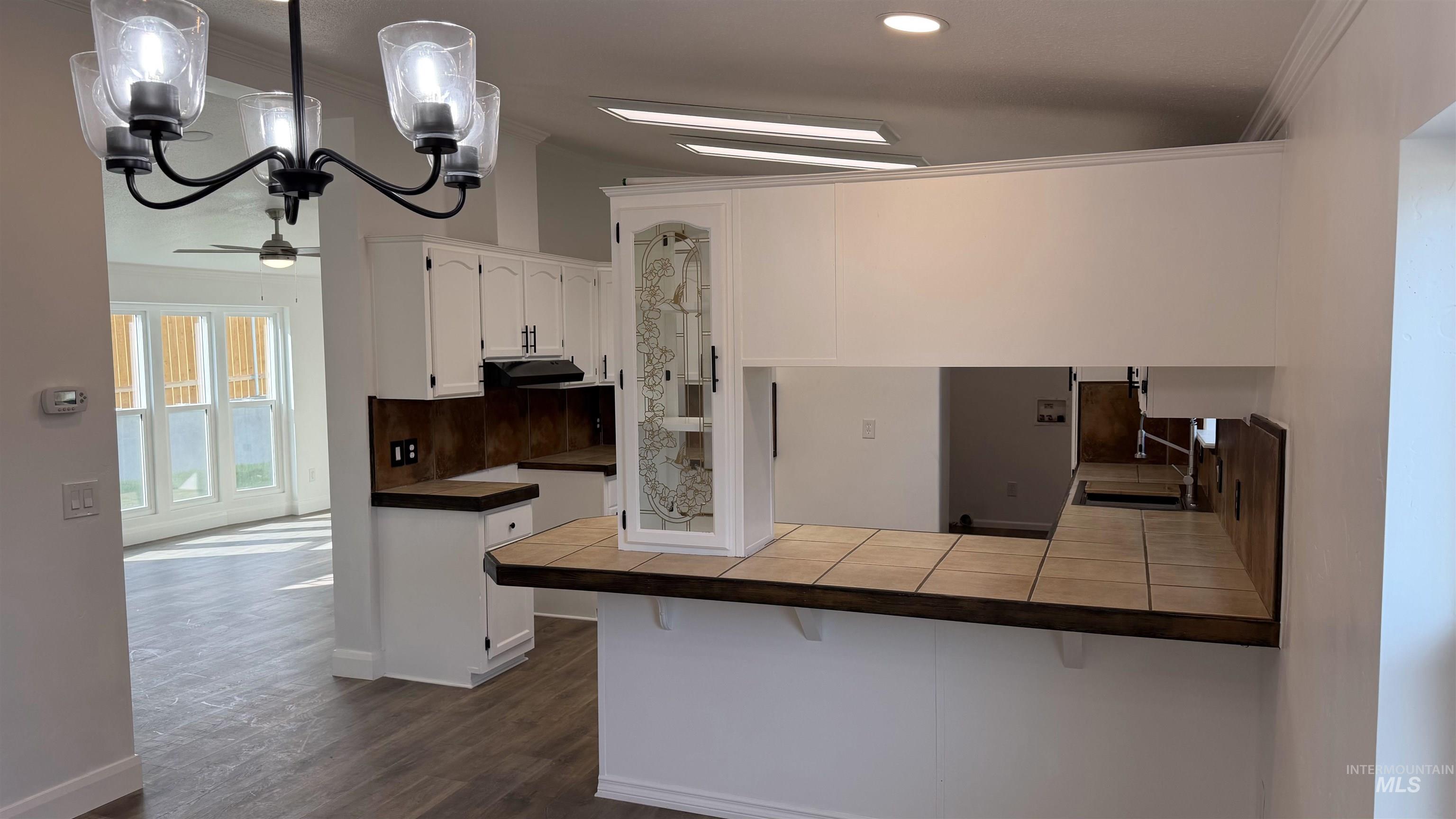 Kitchen featuring tile countertops, a kitchen breakfast bar, white cabinetry, a peninsula, and crown molding