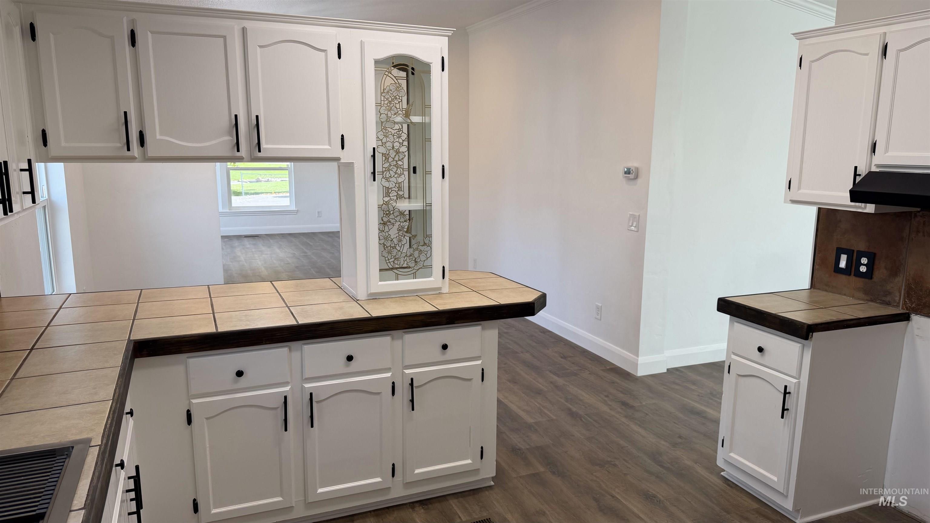 Kitchen with white cabinets, a peninsula, dark wood-style flooring, under cabinet range hood, and crown molding