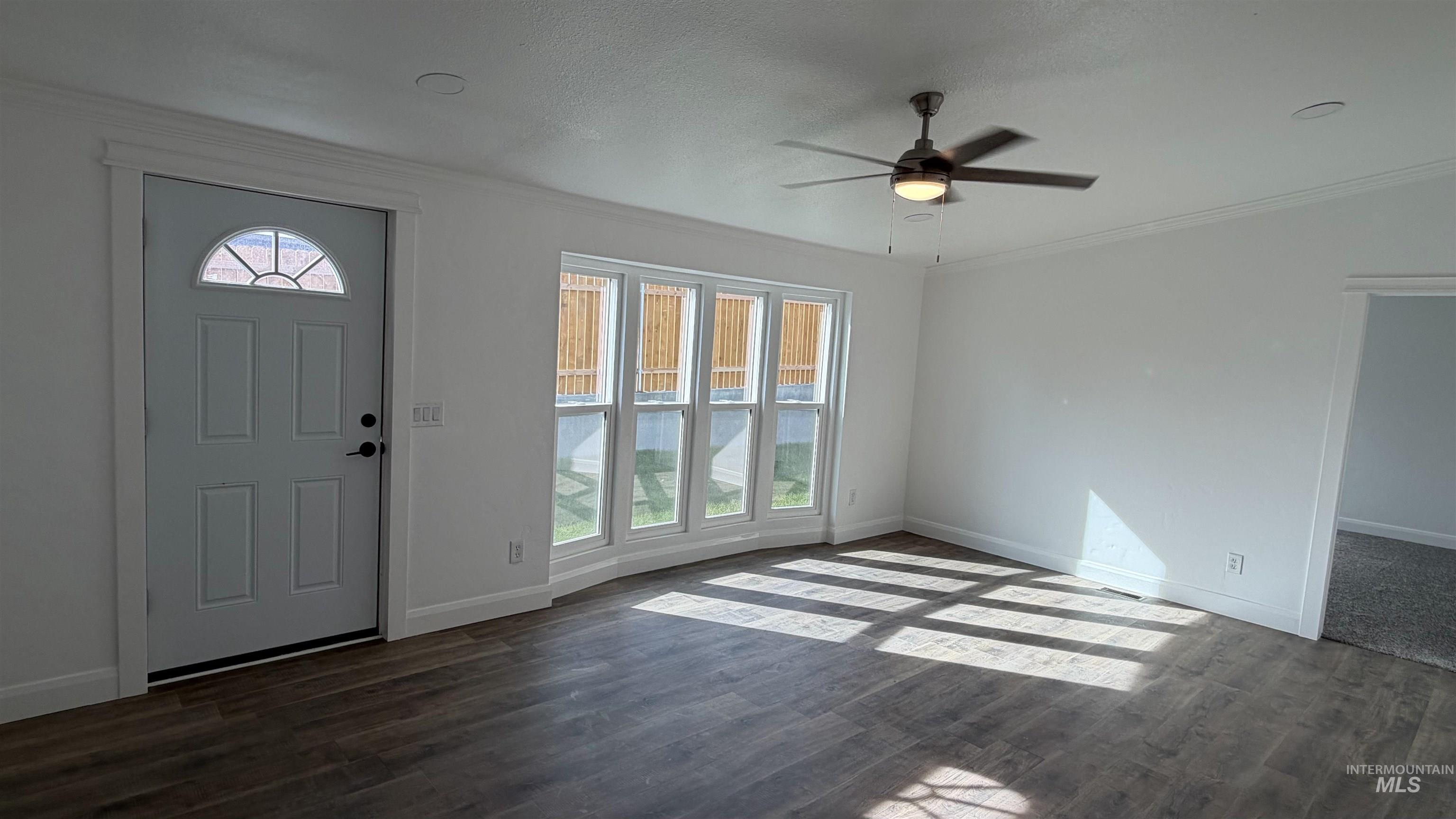 Foyer entrance featuring healthy amount of natural light, crown molding, dark wood-style floors, ceiling fan, and a textured ceiling