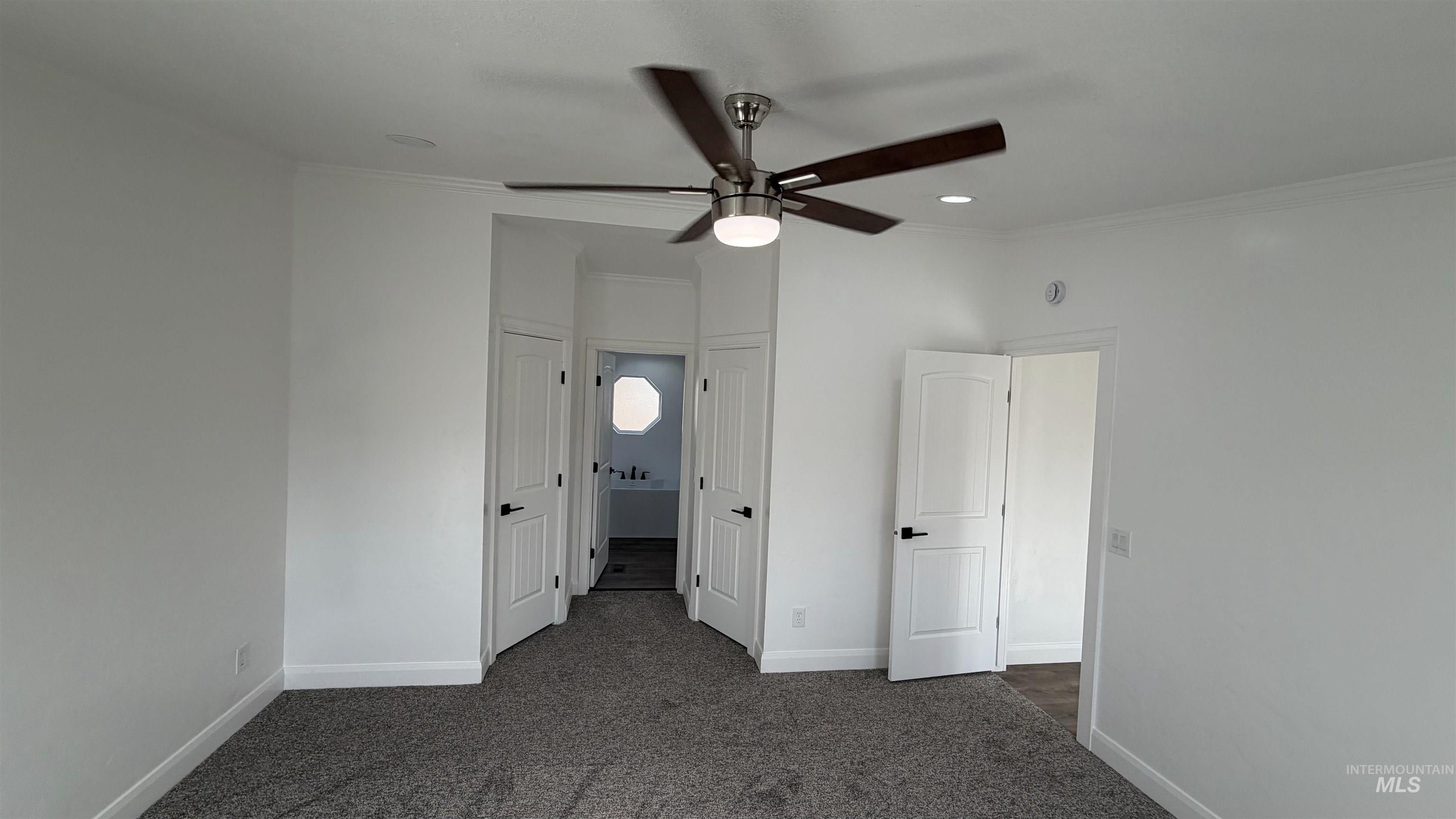 Unfurnished bedroom with ornamental molding, dark carpet, ceiling fan, and ensuite bathroom
