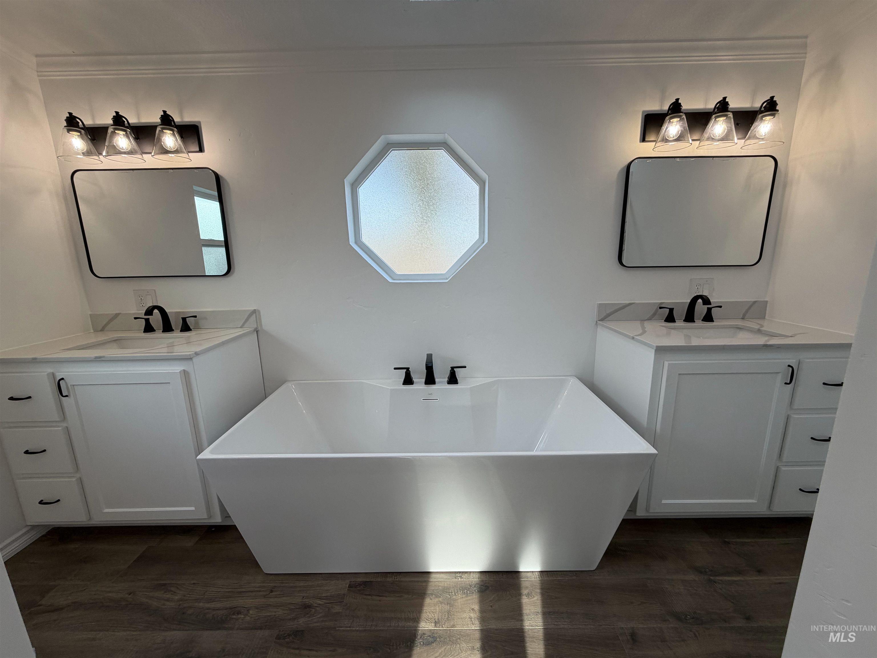 Full bath featuring two vanities, a freestanding tub, dark wood-type flooring, and ornamental molding
