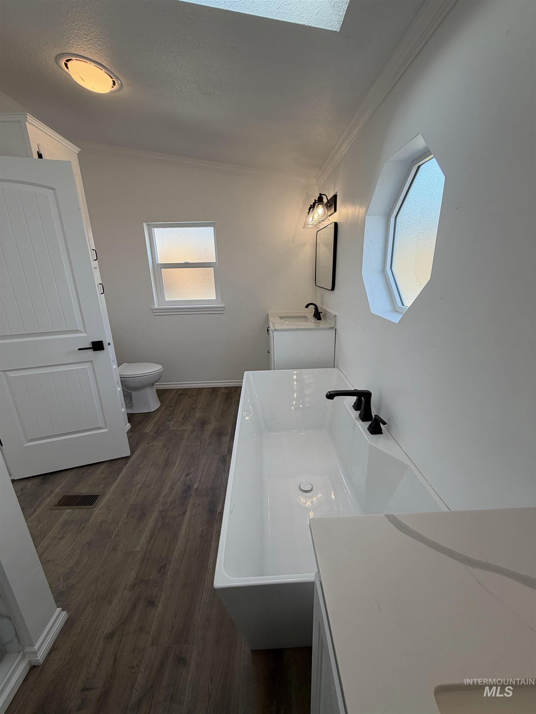 Full bath featuring two vanities, dark wood-style floors, plenty of natural light, a freestanding tub, and lofted ceiling