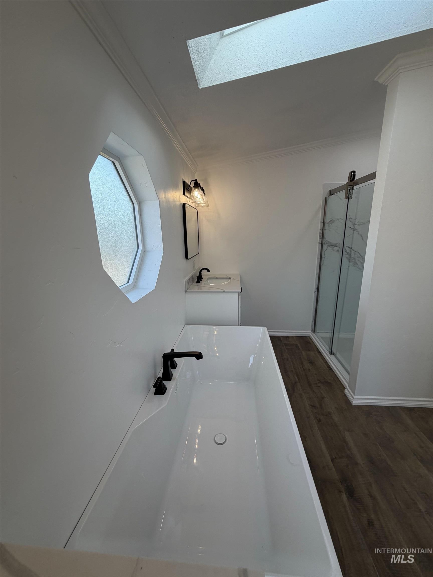 Bathroom featuring ornamental molding, vanity, a marble finish shower, dark wood finished floors, and a skylight