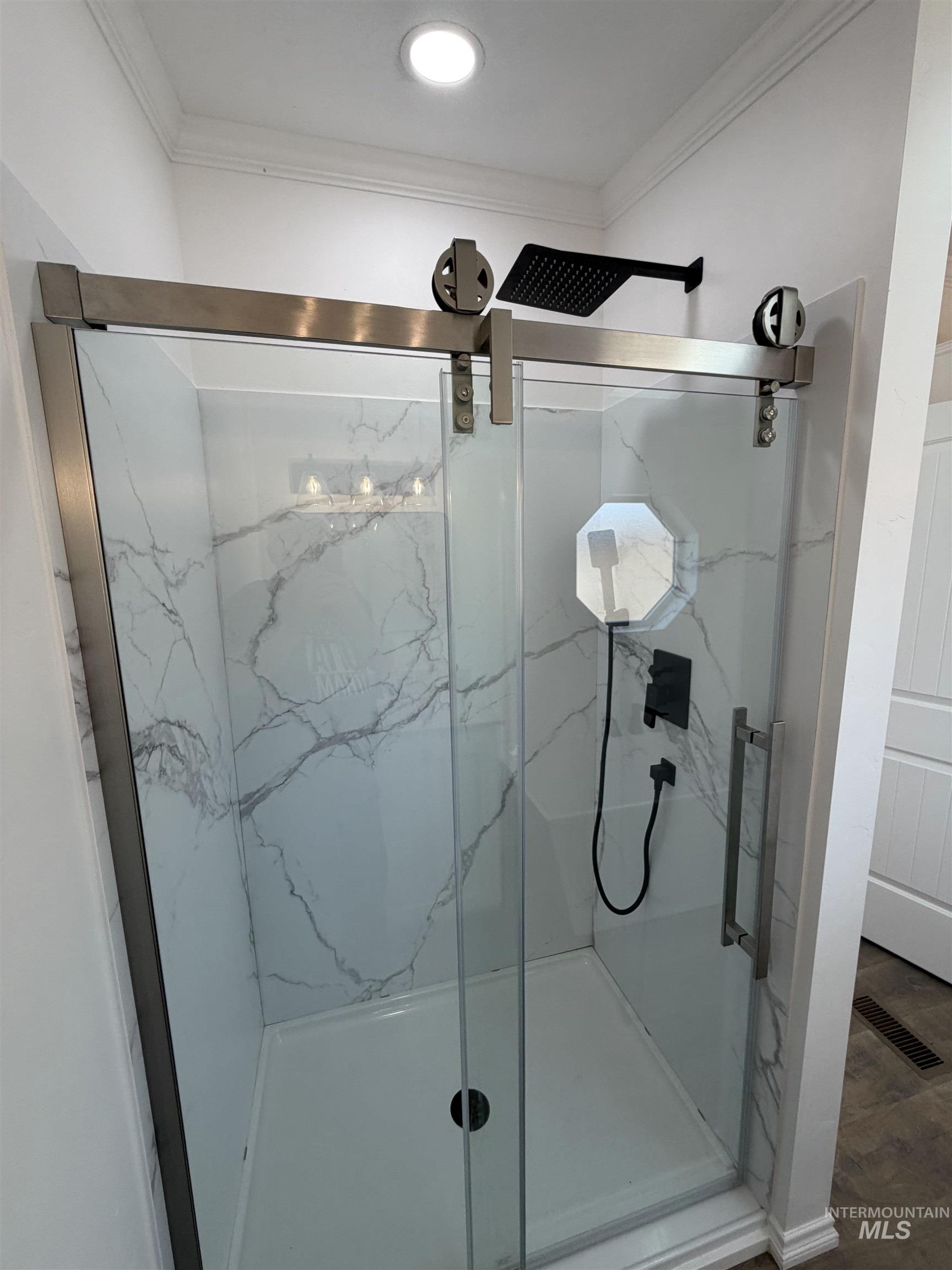 Bathroom featuring ornamental molding, a marble finish shower, and wood finished floors