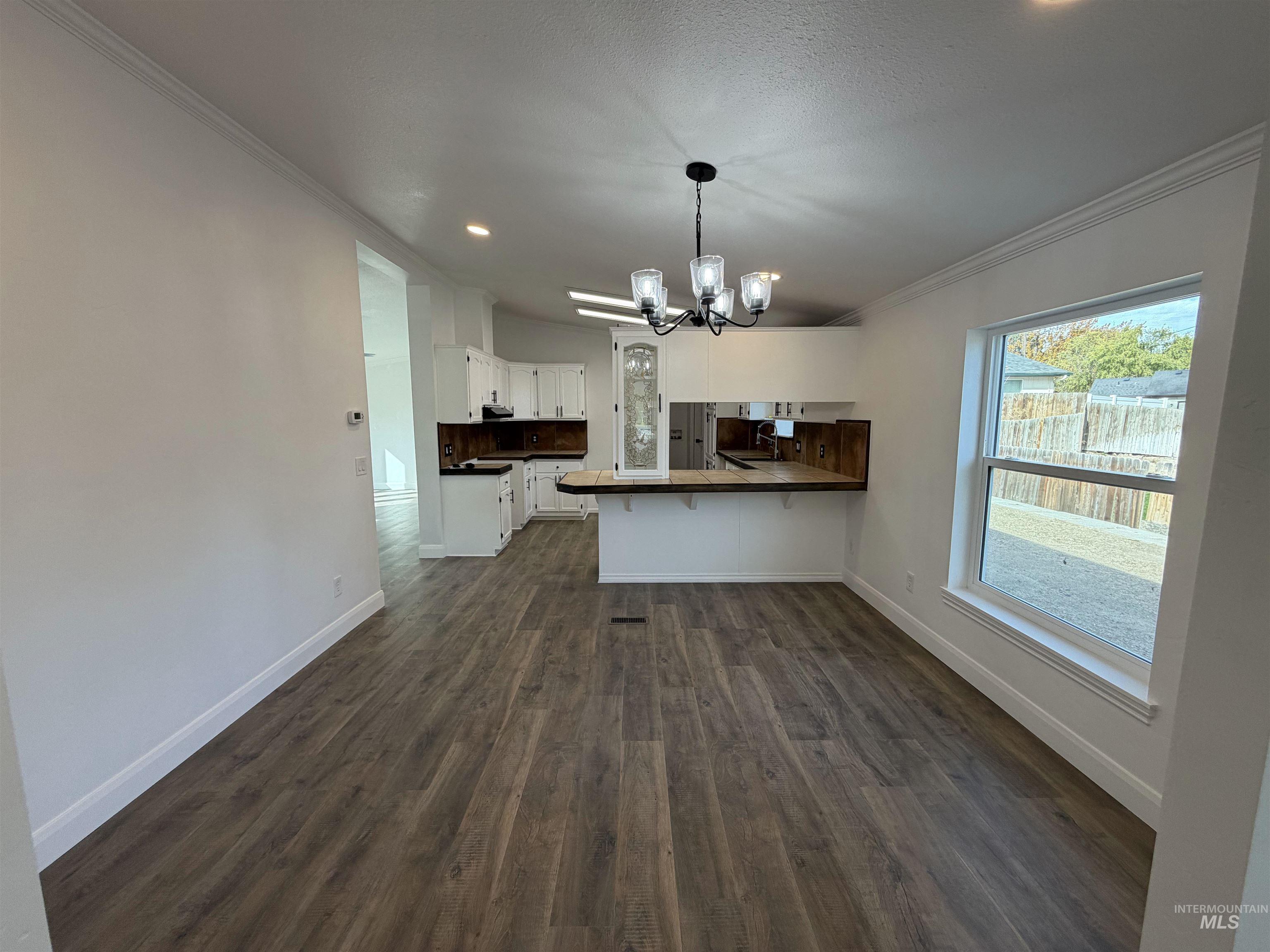 Kitchen featuring a peninsula, ornamental molding, dark countertops, dark wood-style floors, and a chandelier