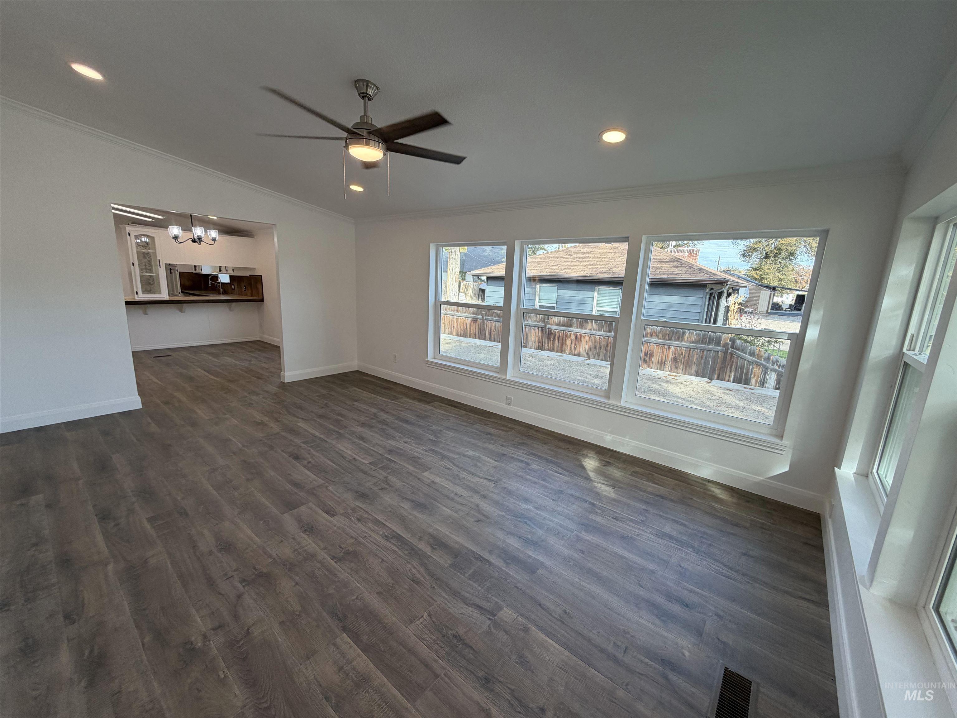 Unfurnished living room with crown molding, recessed lighting, dark wood-style floors, a ceiling fan, and a chandelier