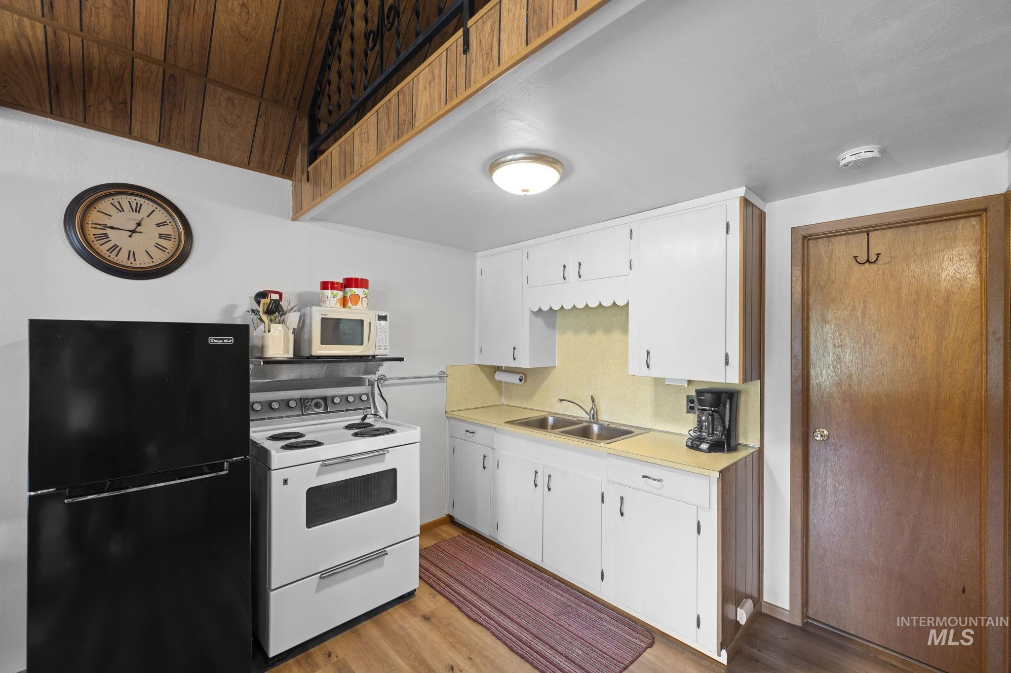 Kitchen with white appliances, light countertops, light wood-type flooring, white cabinets, and backsplash