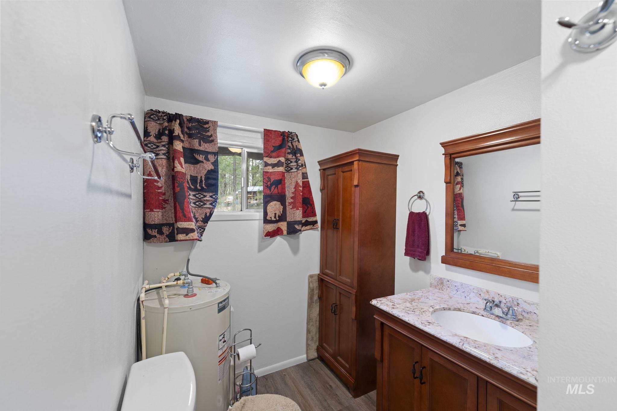 Half bathroom with water heater, dark wood-type flooring, and vanity