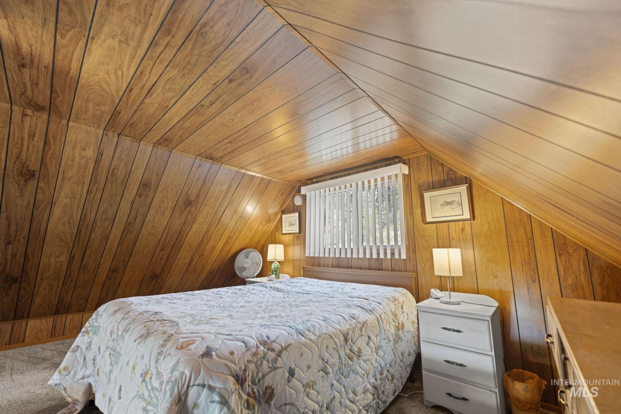 Bedroom featuring wooden ceiling, carpet flooring, wood walls, and lofted ceiling