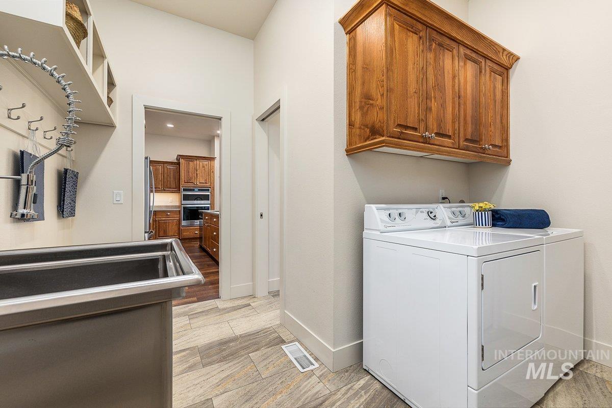 Laundry room with cabinet space, washing machine and dryer, storage closet, laundry sink, and ironing board