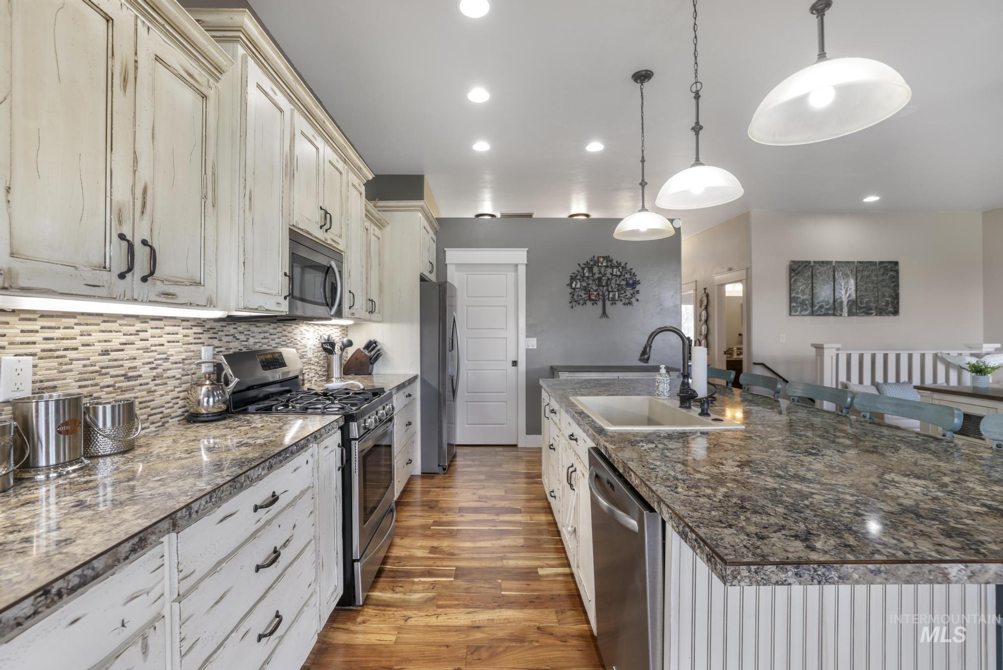 Kitchen featuring appliances with stainless steel finishes, a spacious island, light wood finished floors, hanging light fixtures, and decorative backsplash