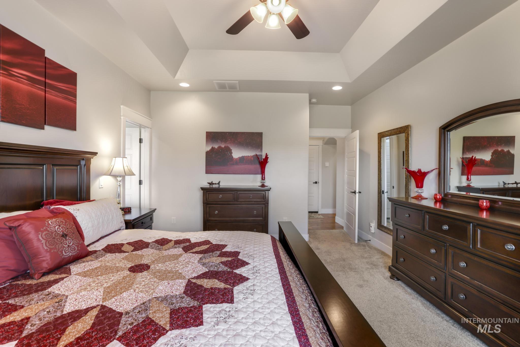 Bedroom with light carpet, ceiling fan, a tray ceiling, and recessed lighting