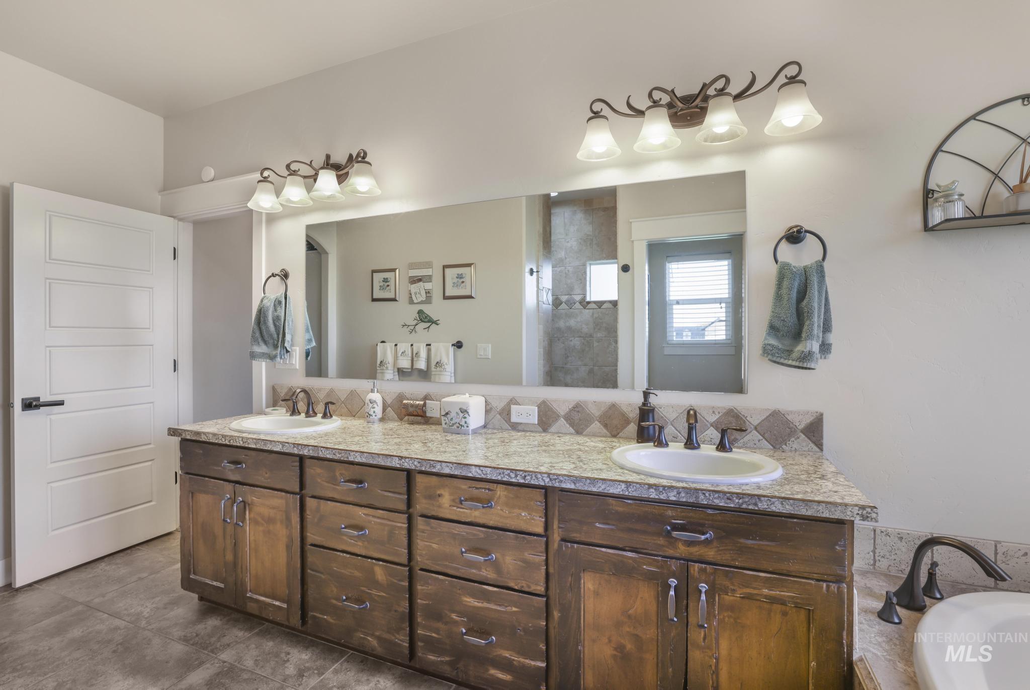Full bath featuring double vanity, a tub to relax in, tiled shower, and dark tile patterned flooring