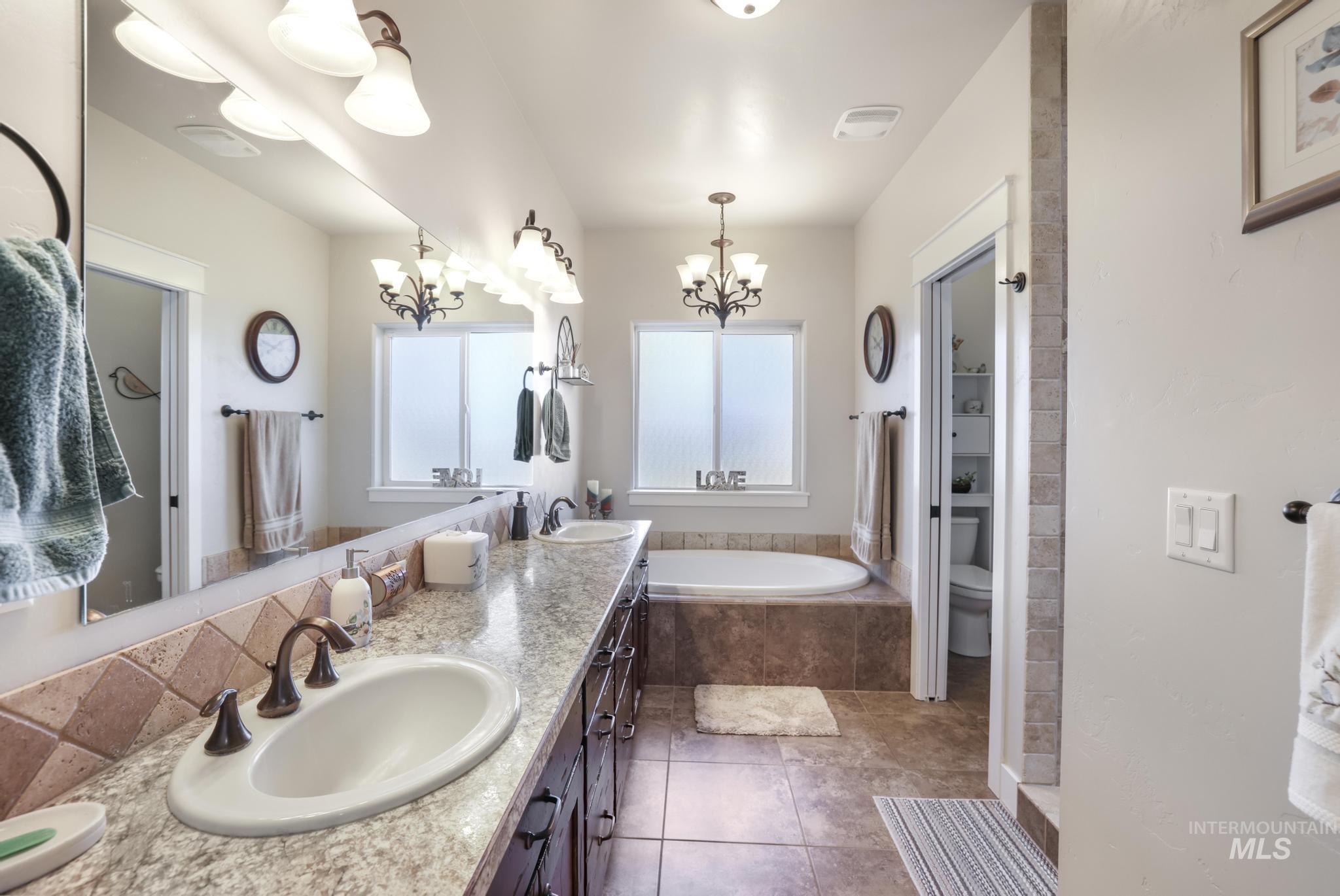 Bathroom with double vanity, a bath, dark tile patterned flooring, and a chandelier