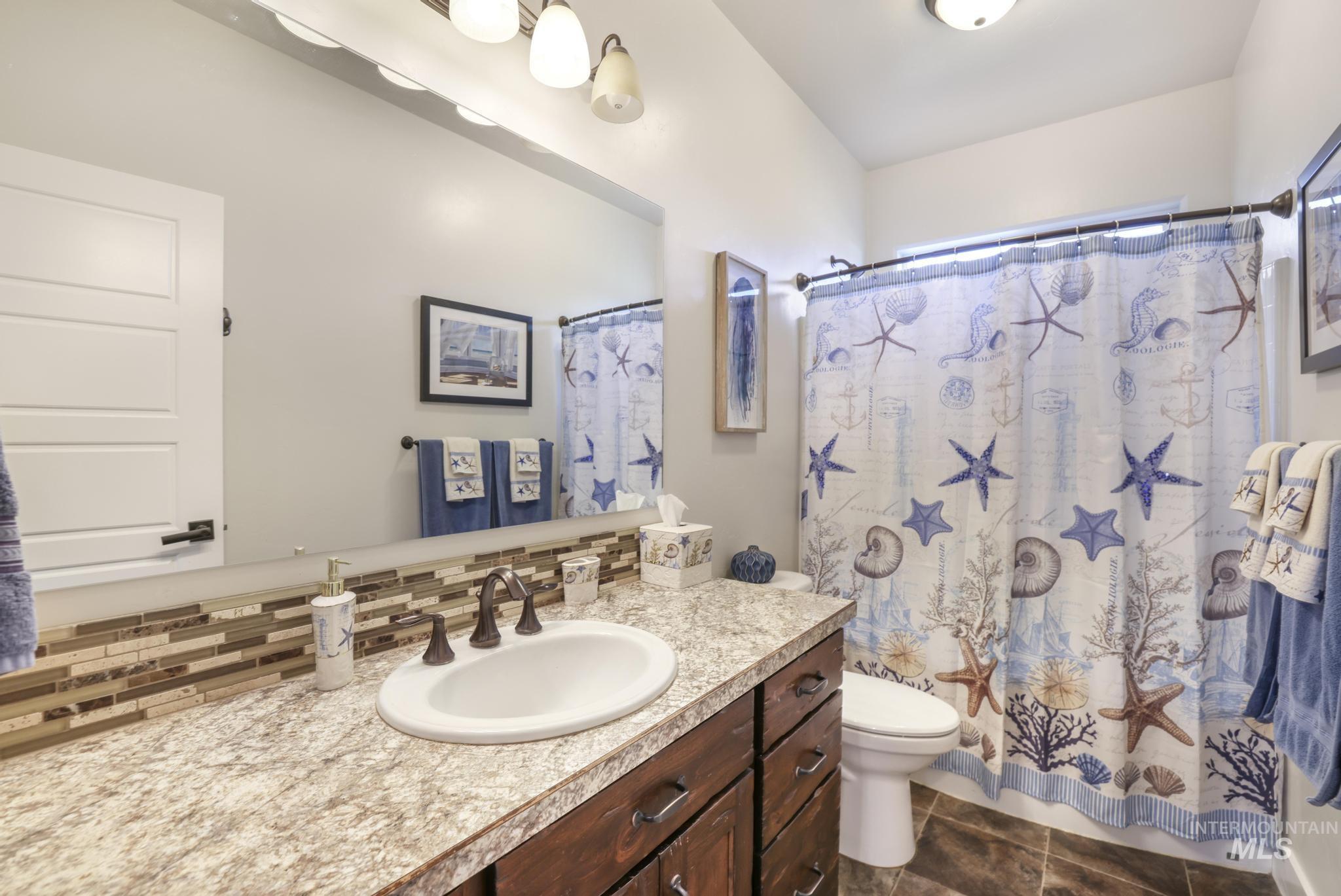 Full bath featuring vanity, a shower with shower curtain, tasteful backsplash, and dark tile patterned flooring