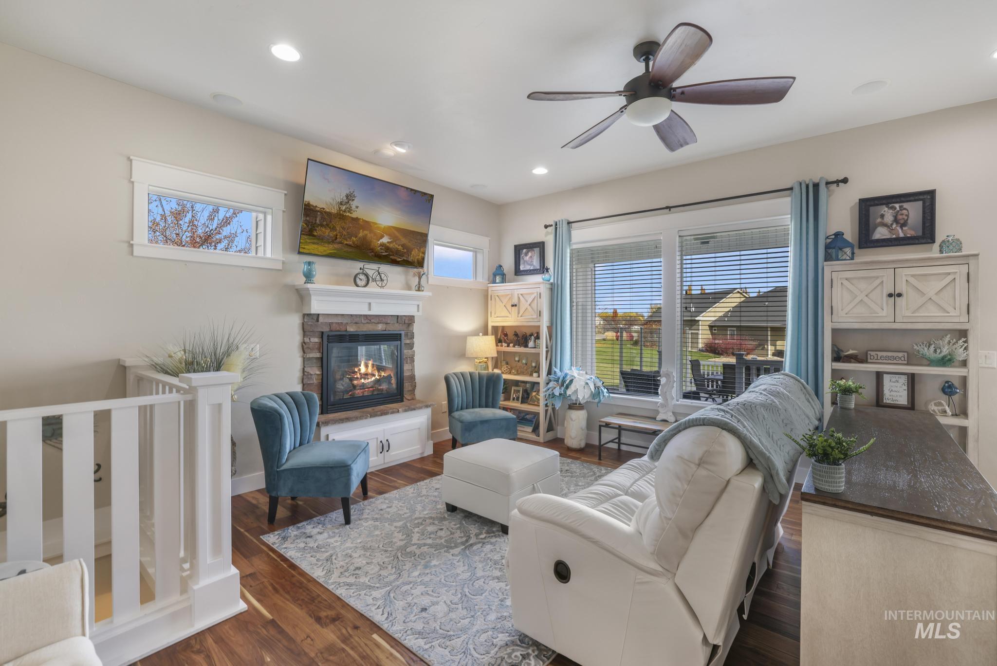 Living room featuring dark wood-style flooring, recessed lighting, a ceiling fan, and a stone fireplace